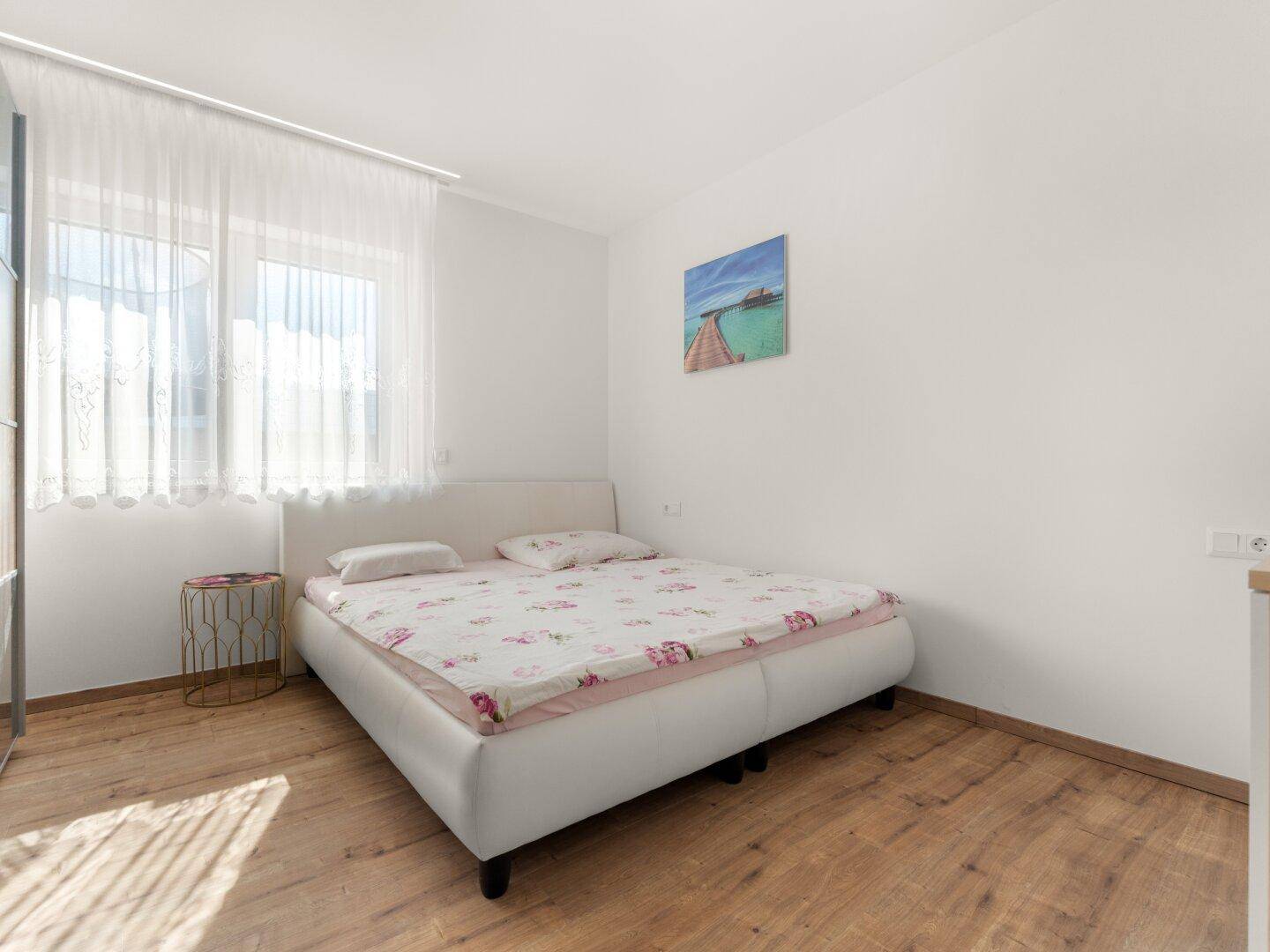 Schlafzimmer mit Doppelbett, Holzboden und großem Fenster für viel Tageslicht.