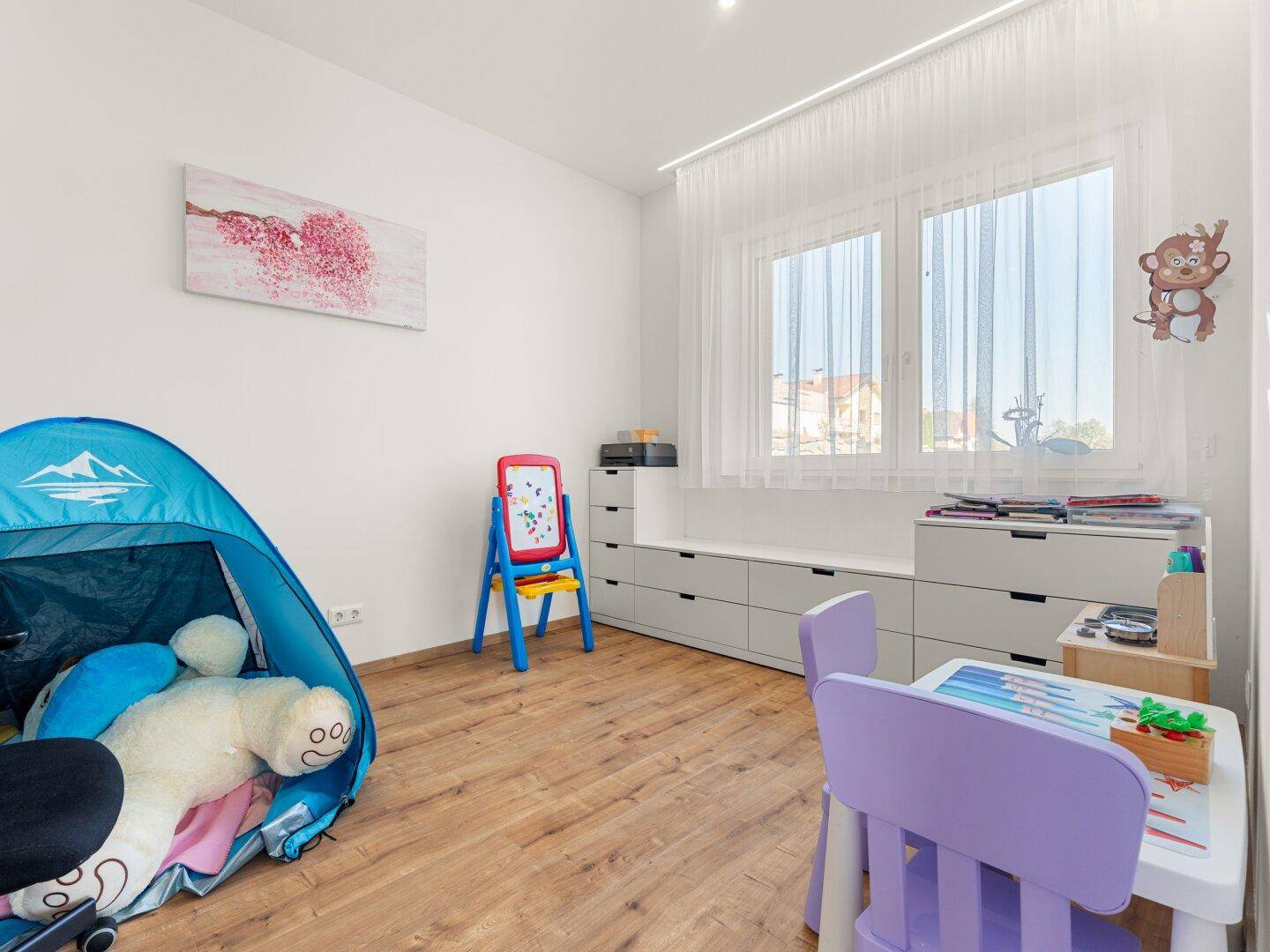 Helles Kinderzimmer mit Spielbereich, Holzboden und großem Fenster.