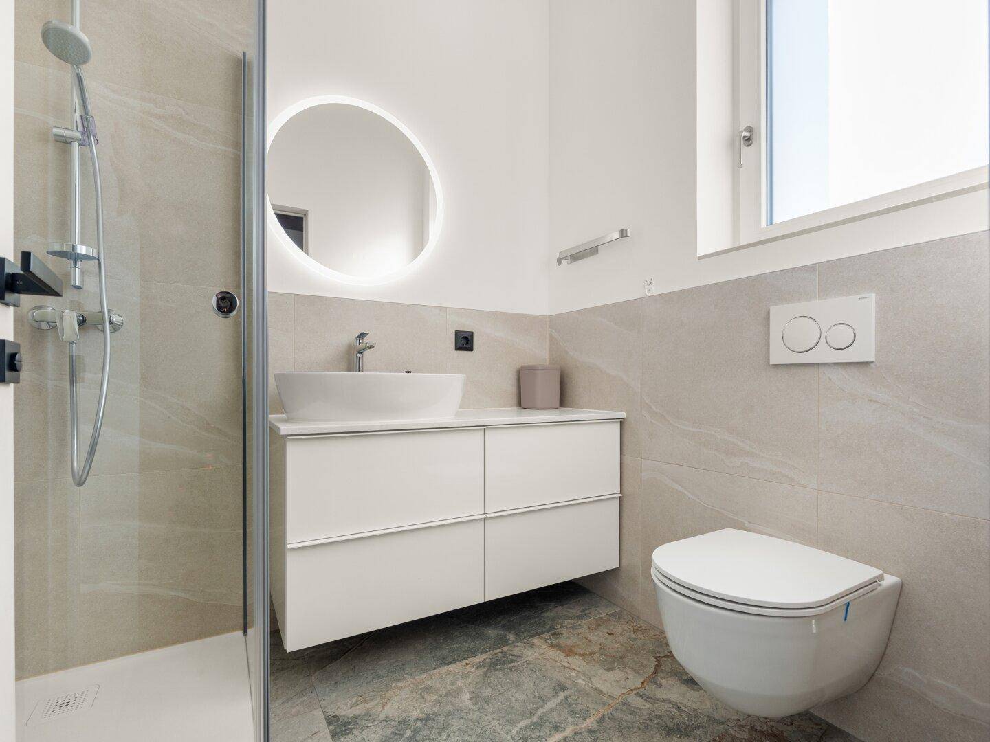 Modernes Badezimmer mit begehbarer Dusche, Wand-WC und beleuchtetem Spiegel.