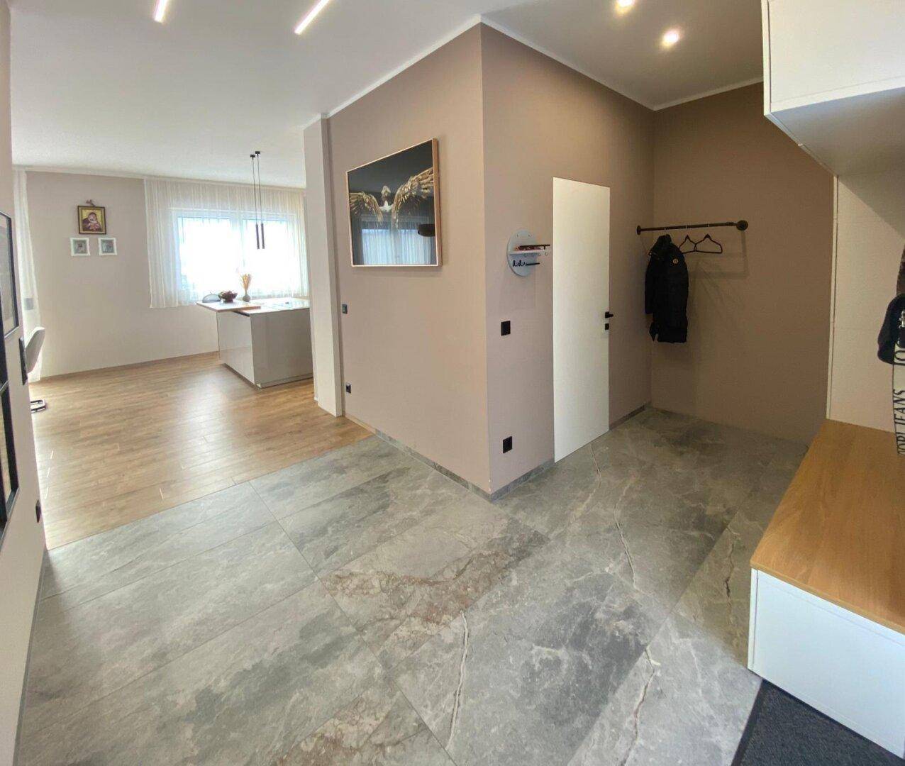 Heller Eingangsbereich mit Fliesenboden und Garderobe, offen zum Wohnbereich.
