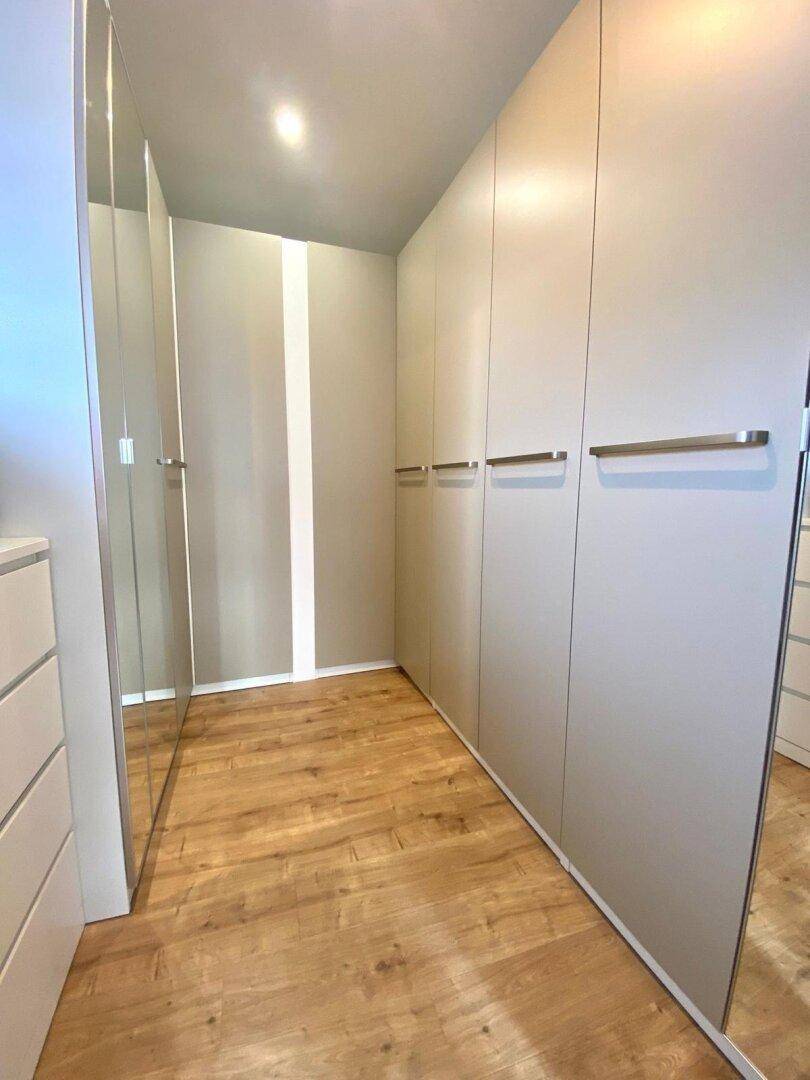 Geräumiger begehbarer Kleiderschrank mit Spiegeltüren und Holzboden.