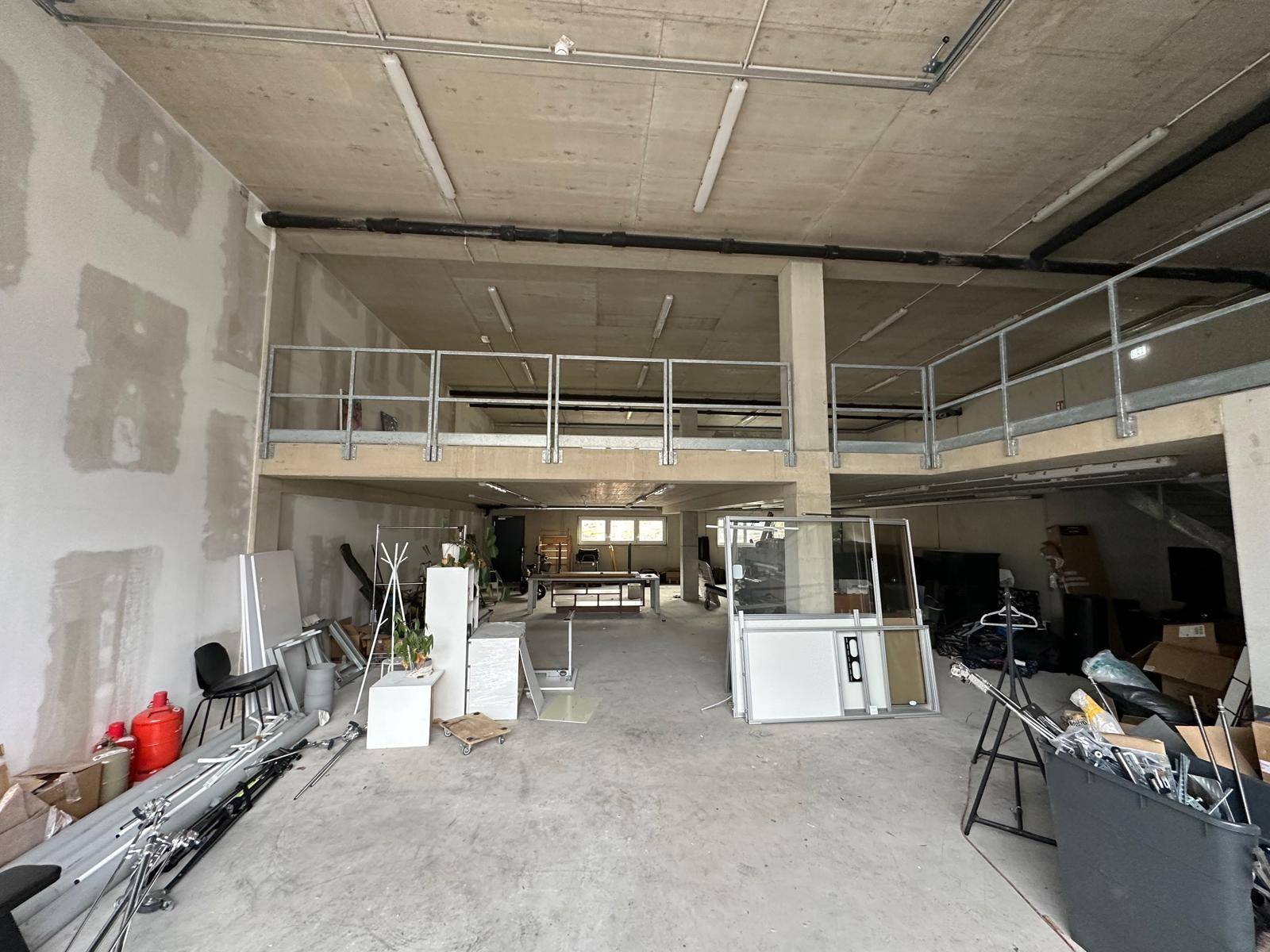 Großer offener Raum mit einer Galerieebene, Betonboden und unfertigen Wänden.