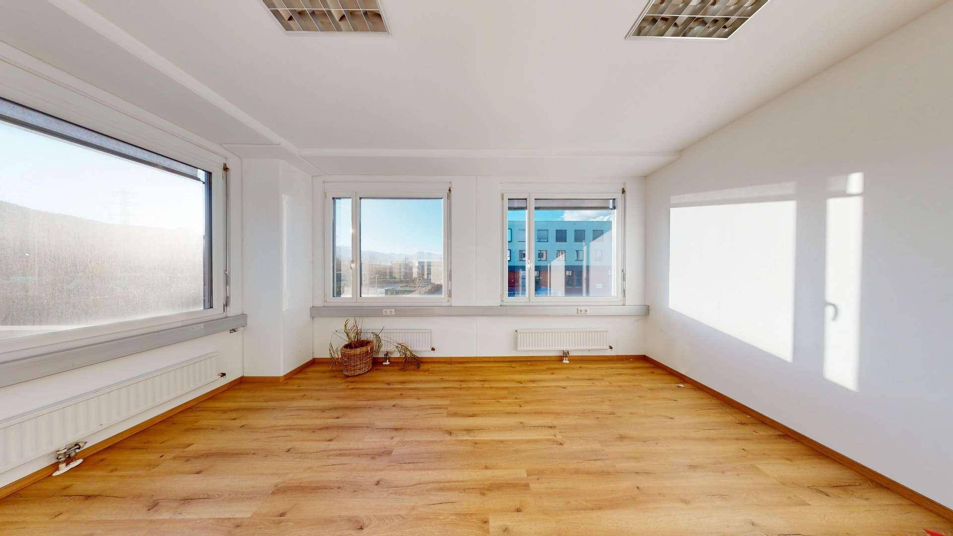 Heller, leerer Büroraum mit mehreren Fenstern, Laminatboden und Blick auf umliegende Gebäude, gut gepflegt.