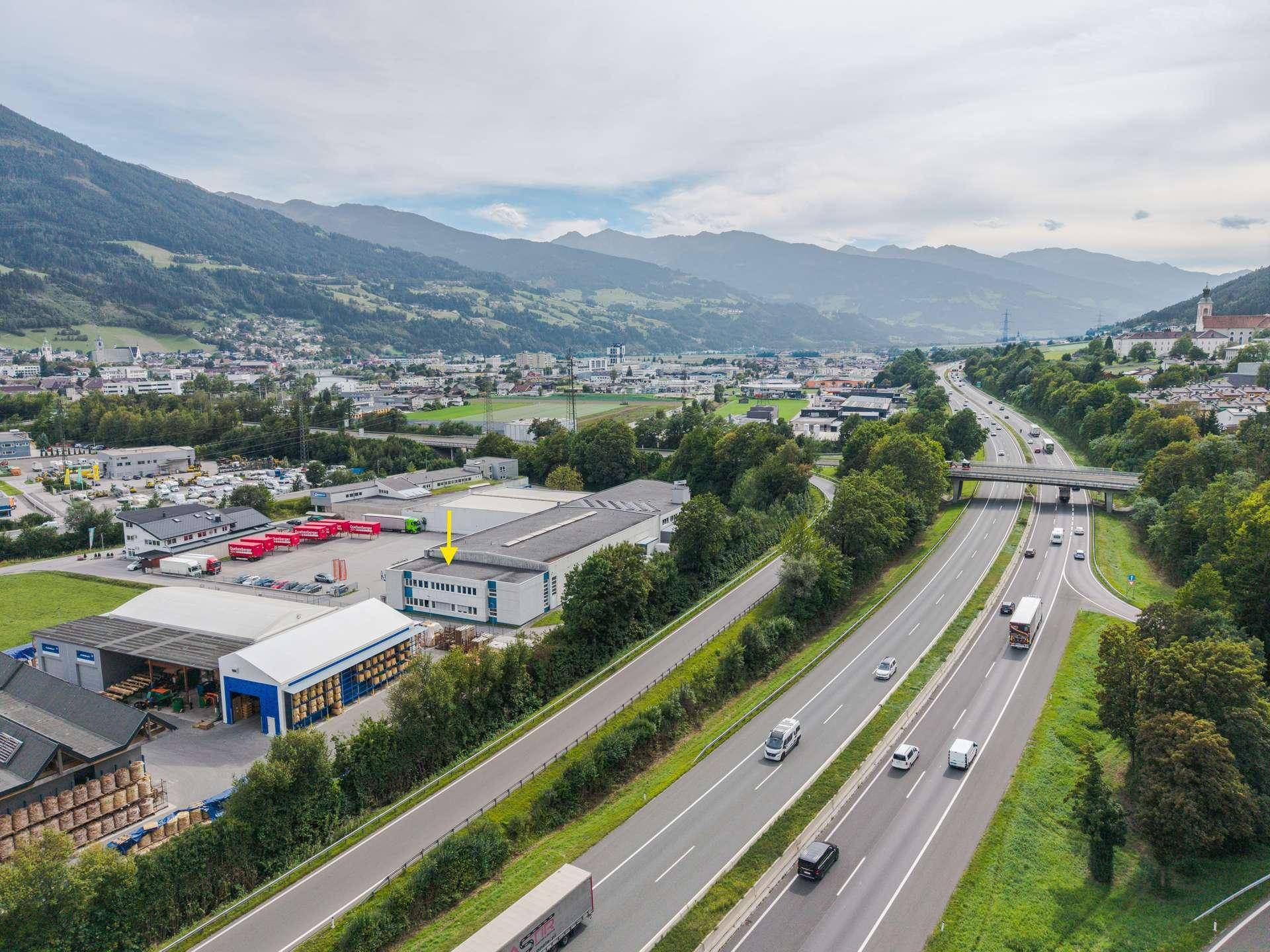 Weitläufige Luftaufnahme des Gewerbegebiets mit Autobahnanbindung und malerischer Bergkulisse.
