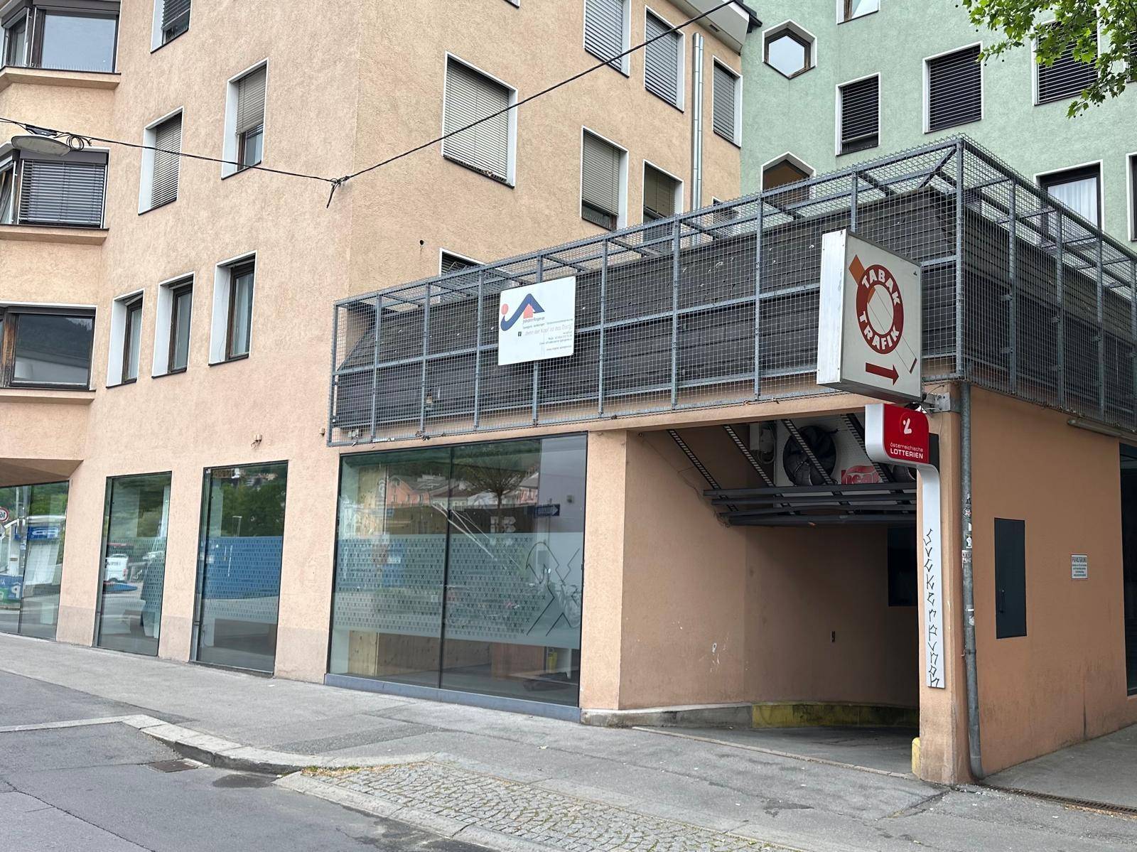 Fassade eines Gebäudes mit Geschäftsflächen im Erdgeschoss und Einfahrt zu einer Tiefgarage.