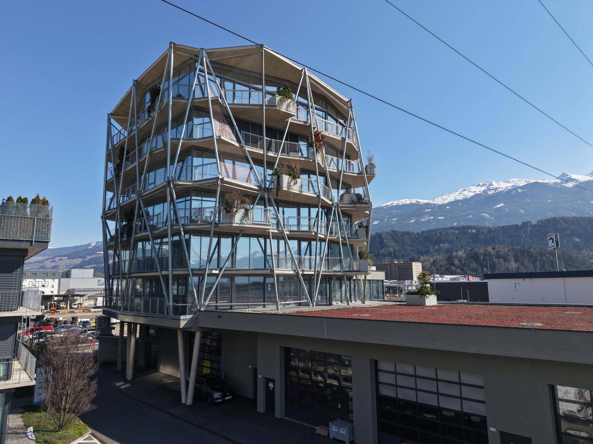 Architektonisch einzigartiges Gebäude mit vielen Glasflächen und einer tragenden Außenstruktur vor einer beeindruckenden Bergkulisse.