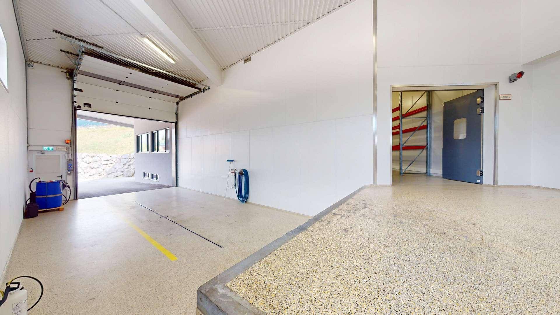 Heller Lagerraum mit großem Rolltor, Industrieboden und Zugang zu weiteren Bereichen.