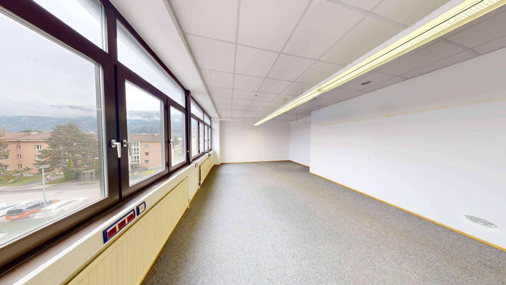 Langes, leeres Büro mit Fensterfront, bietet weite Aussicht und viel Tageslicht für produktives Arbeiten.