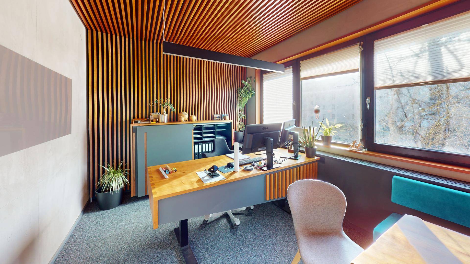 Modern eingerichtetes Büro mit Holzlamellenwand, Schreibtisch und Blick ins Grüne durch große Fenster.