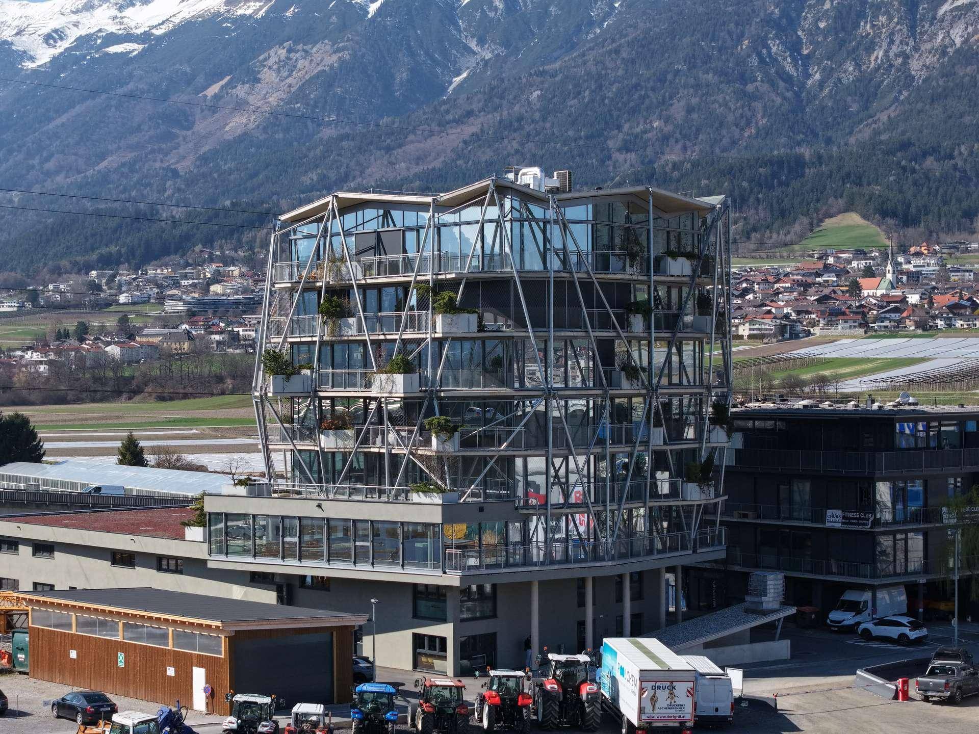 Architektonisch ansprechendes Gebäude mit Glasfassade und Balkonen vor einer beeindruckenden alpinen Kulisse.