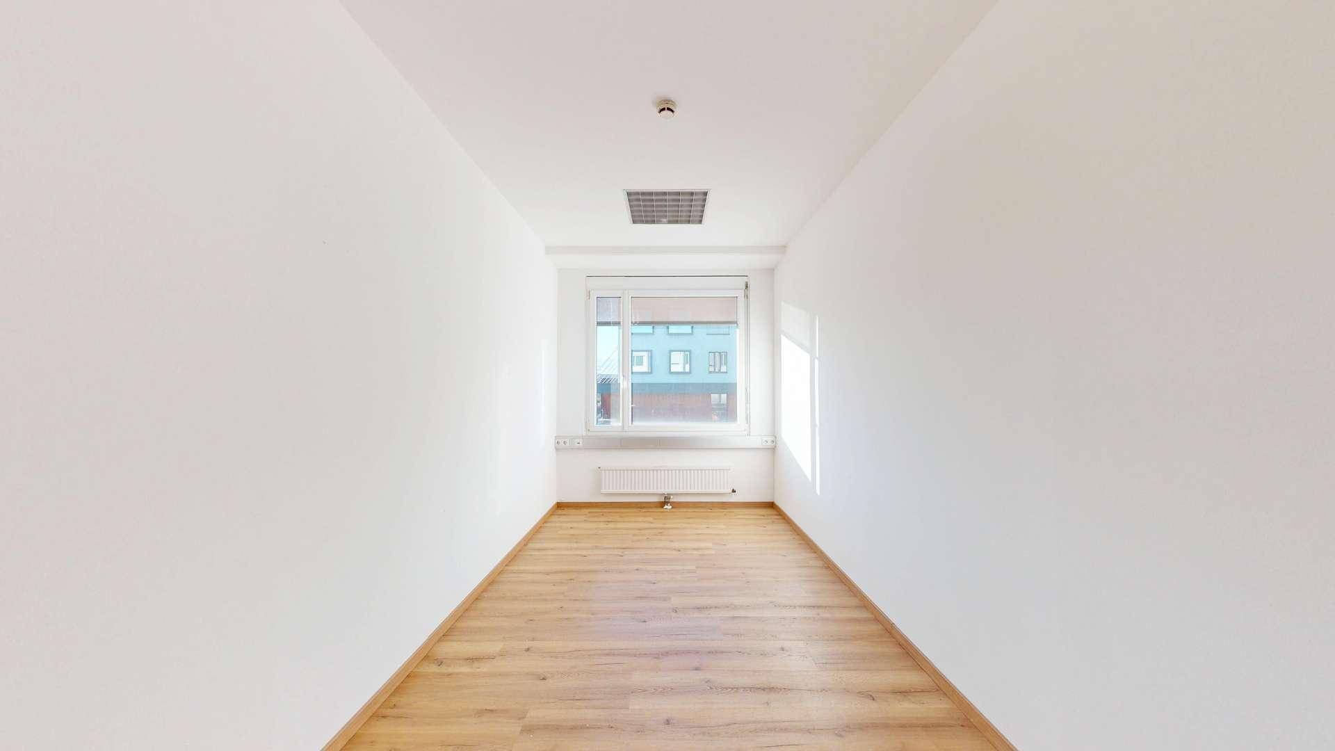 Schmaler, leerer Raum mit hellem Laminatboden und einem Fenster, ideal als kleines Büro oder Besprechungszimmer.