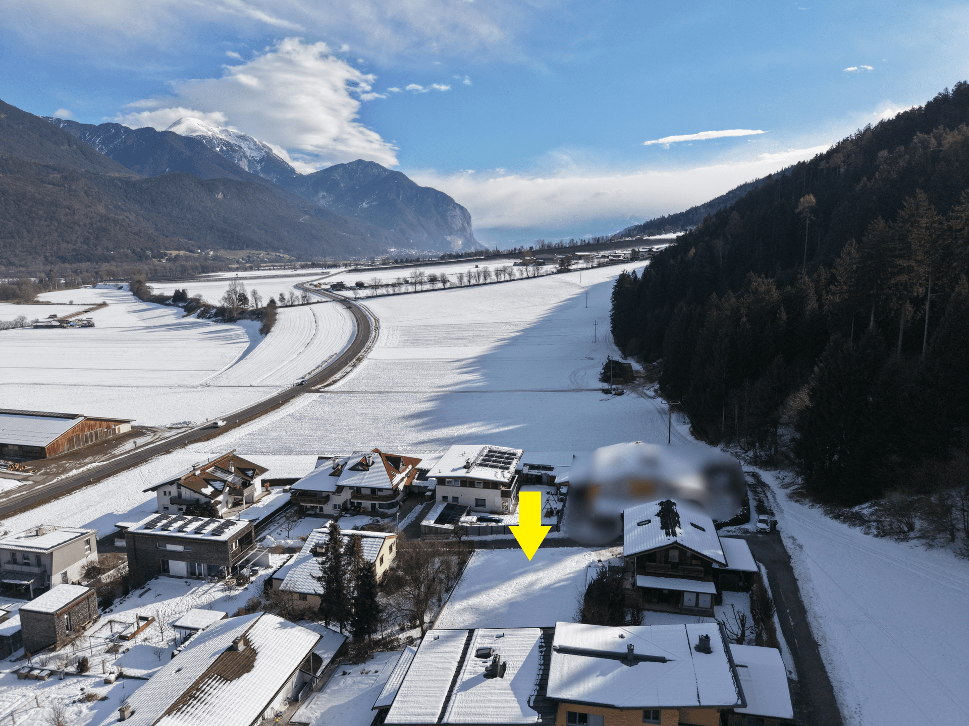 Panoramablick auf das markierte Grundstück in einer verschneiten ländlichen Umgebung mit Bergen und Feldern.