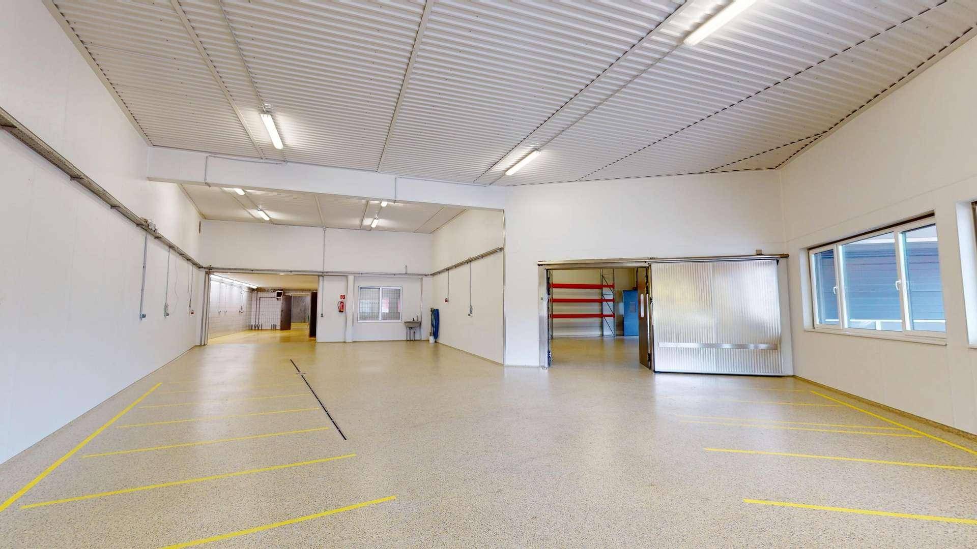 Geräumiger Lagerbereich mit gelben Bodenmarkierungen, Fenstern und Schiebetür zu einem Nebenraum.