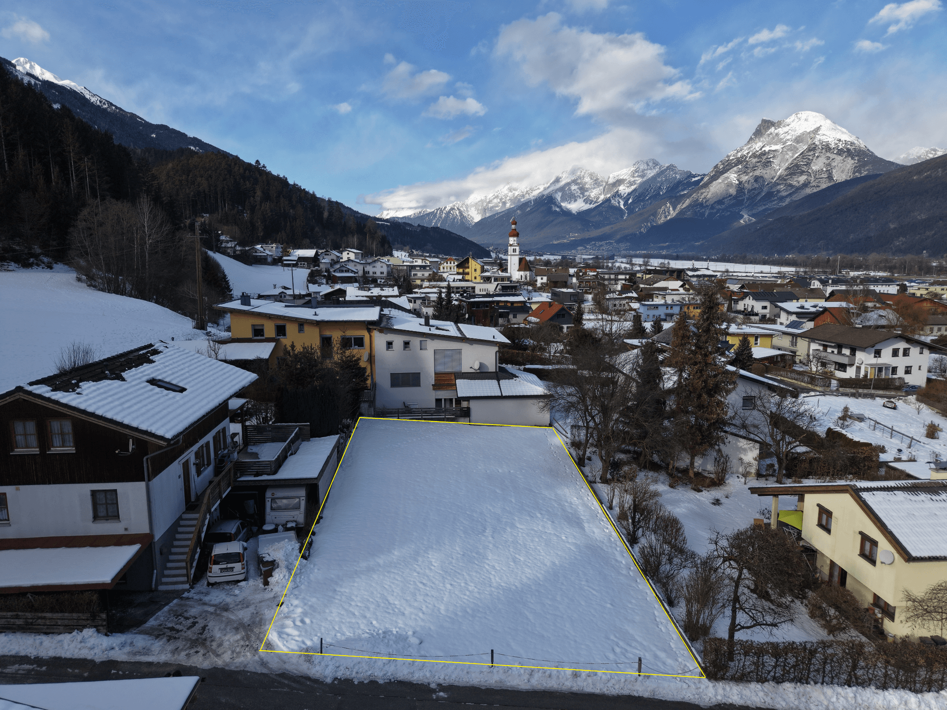 Schneebedecktes Grundstück in einer malerischen Dorflandschaft mit beeindruckendem Bergblick.