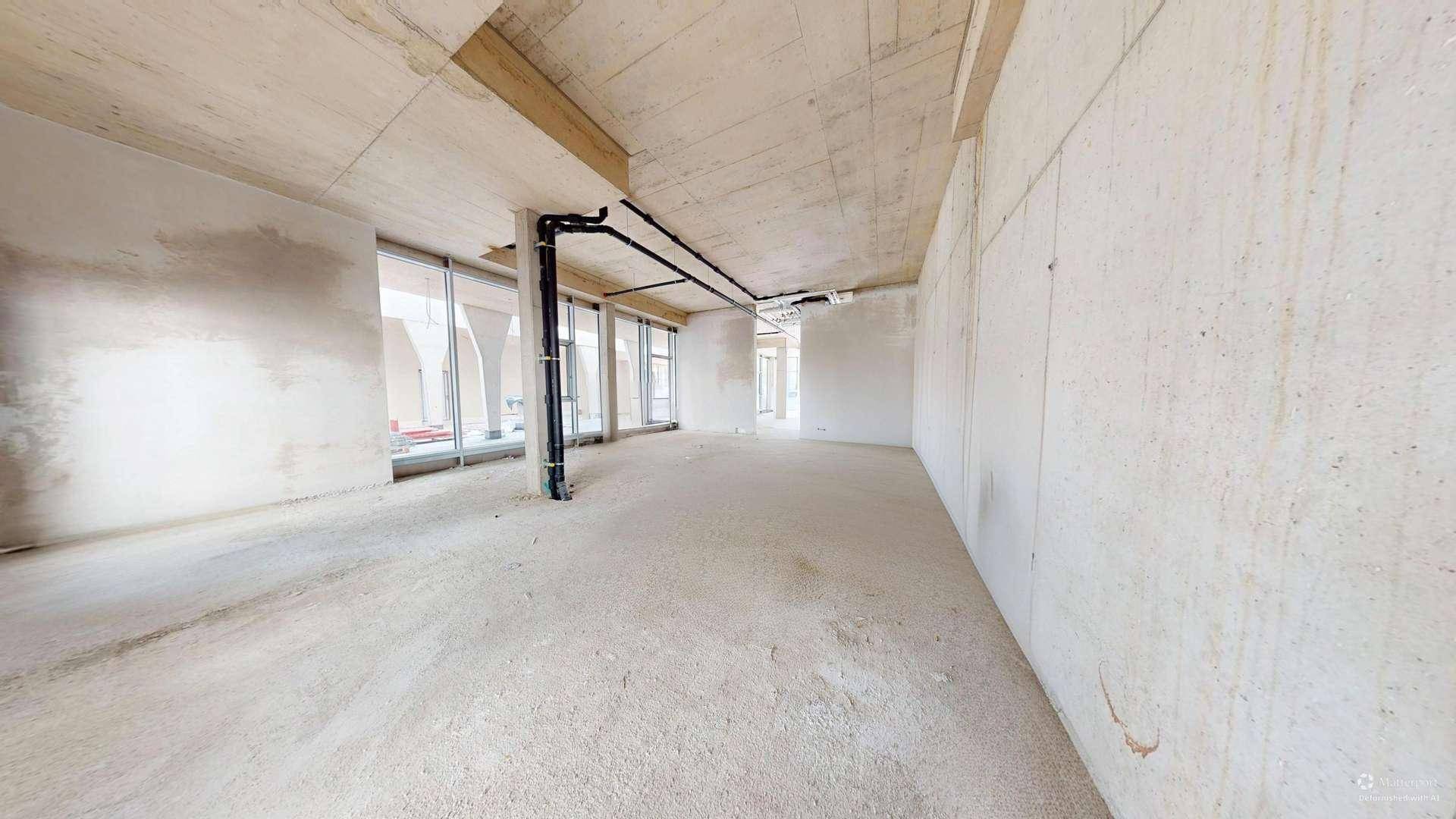 Unfertiger Innenraum mit Betonwänden, hohen Decken und großen Fensterfronten, bereit für den Ausbau.