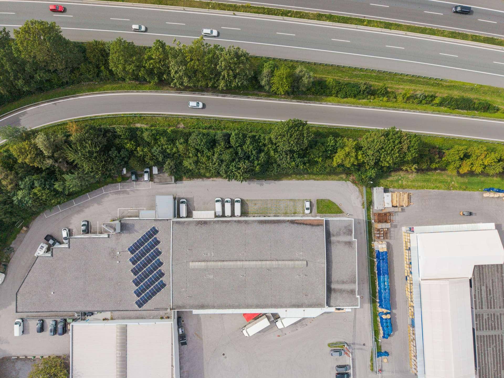 Luftaufnahme des Gewerbegebäudes mit Photovoltaikanlage auf dem Dach und angrenzender Autobahn.