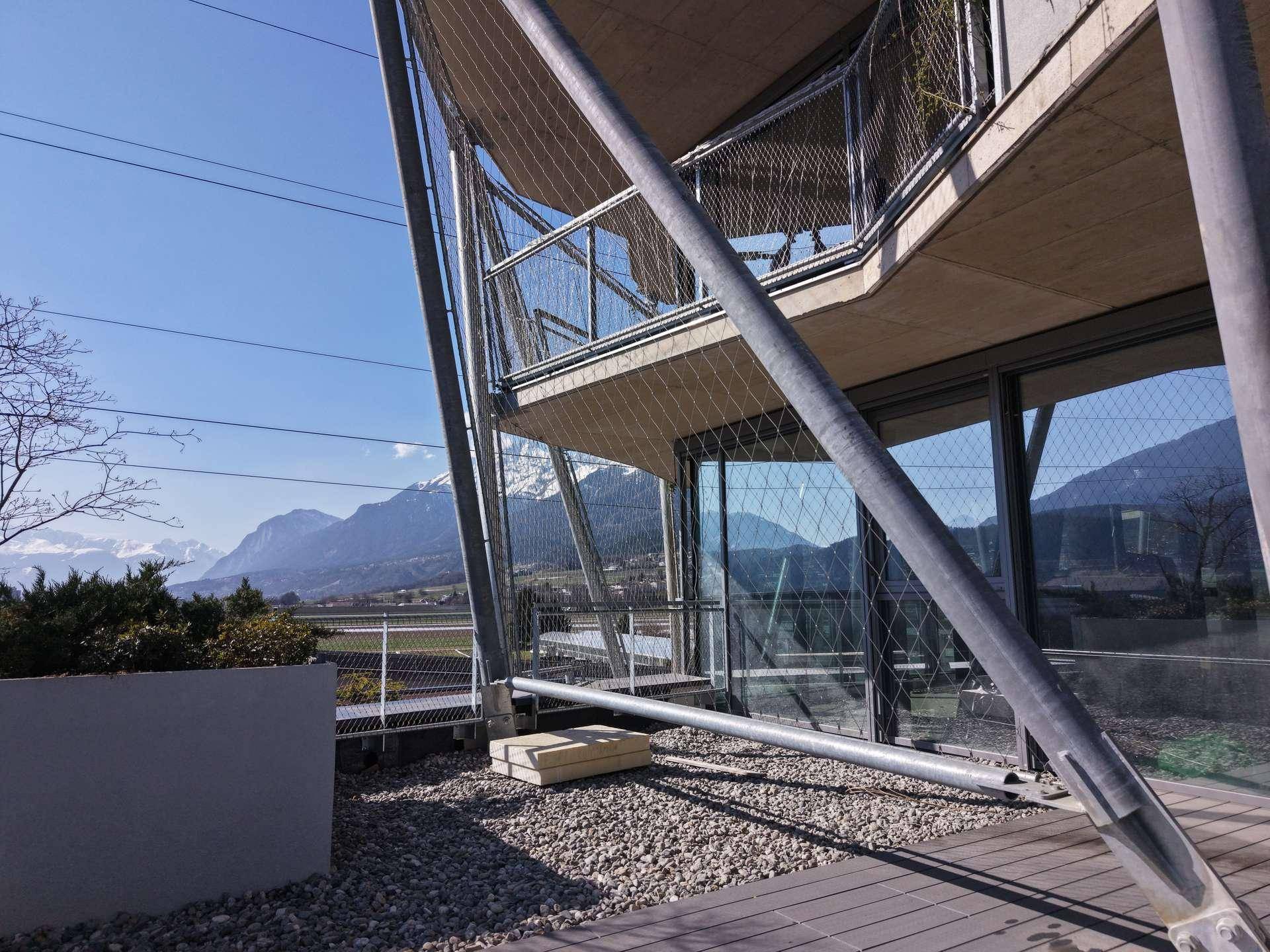 Eine moderne Terrasse mit Holzboden und Kiesflächen, umgeben von einer Drahtseilkonstruktion und Bergblick.