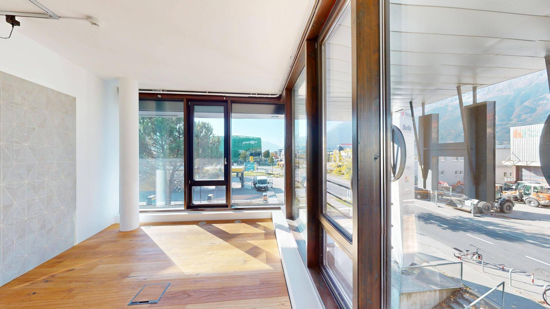 Geräumiger Innenbereich mit großen Fenstern, Holzboden und Blick auf die Straße und Berge.
