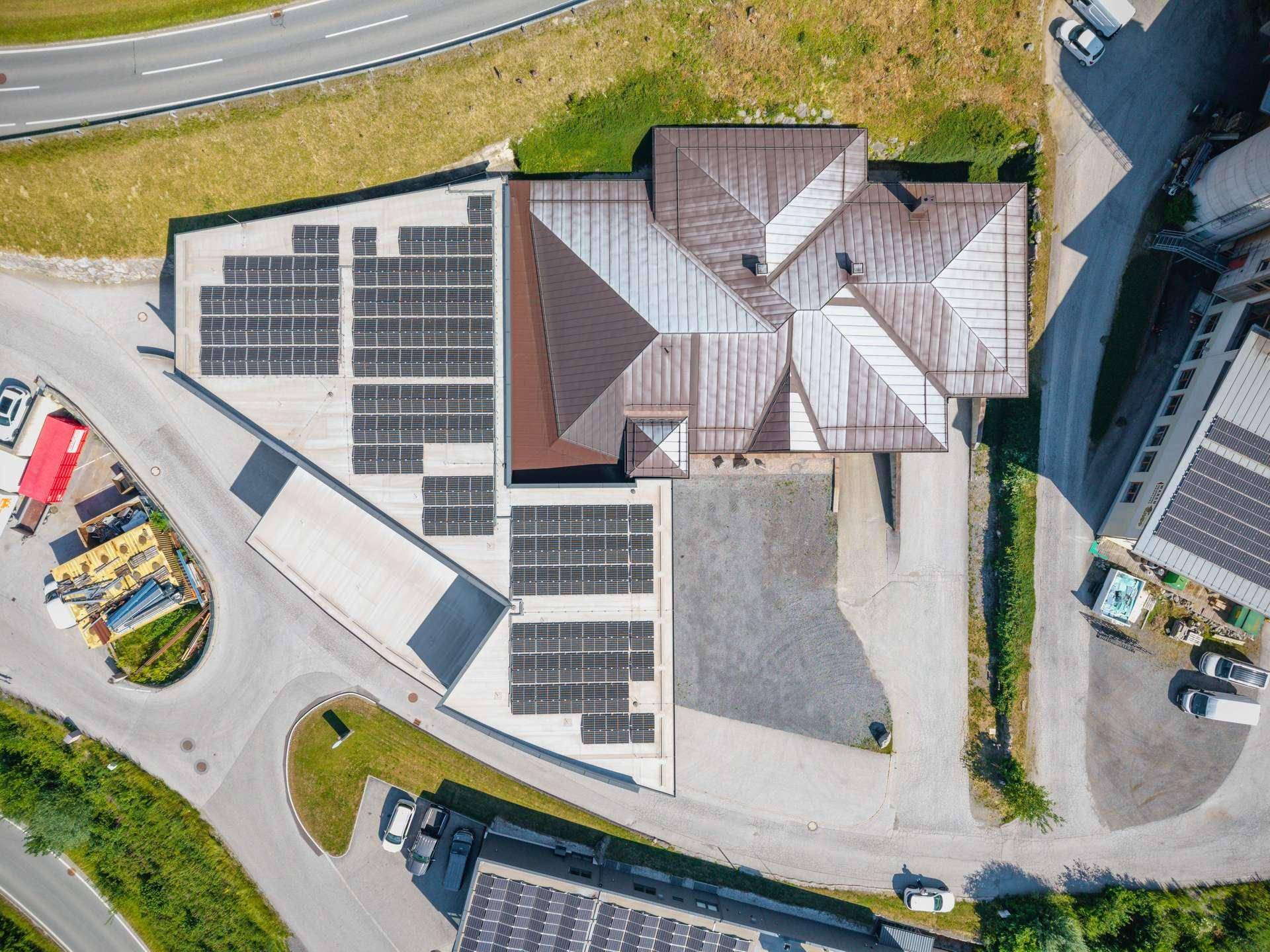 Draufsicht auf ein Gebäude mit Photovoltaik-Anlagen auf dem Dach und umliegenden Parkflächen.