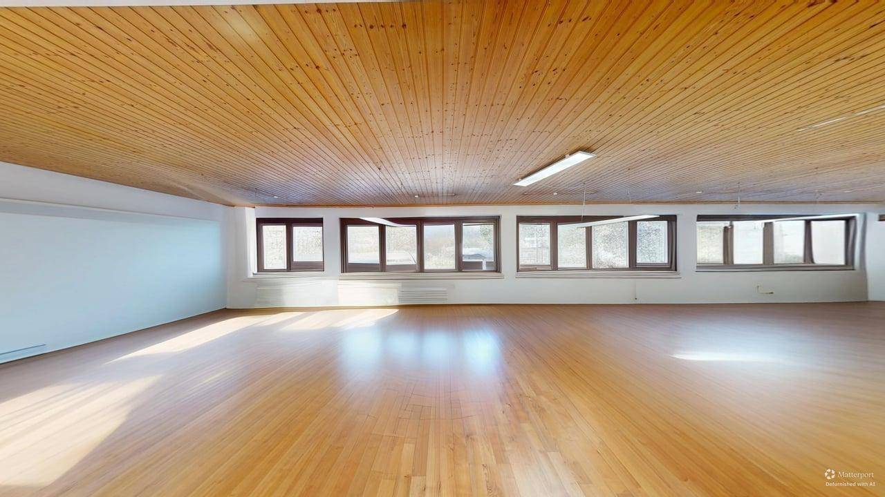 Heller und weitläufiger Büroraum mit durchgehendem Holzboden und Holzdecke sowie vielen Fenstern.