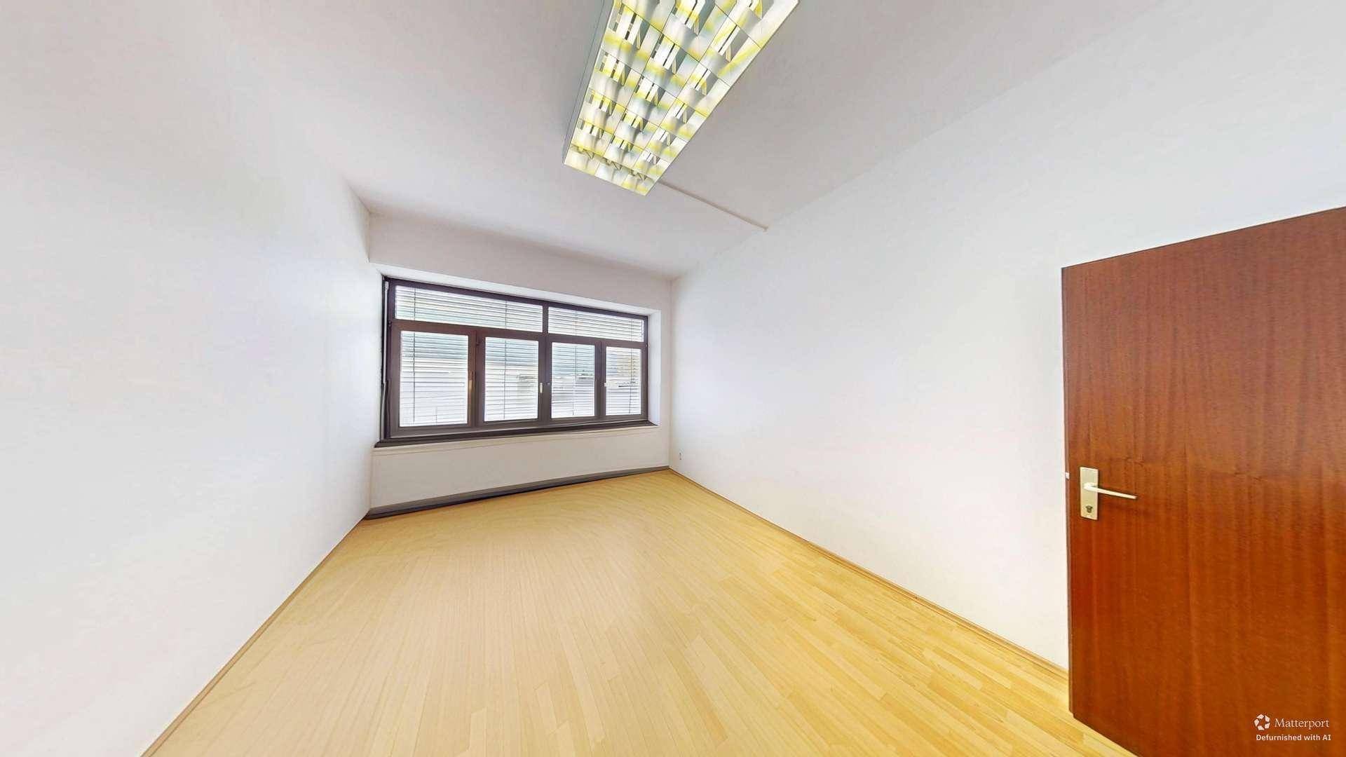 Kleinerer, heller Büroraum mit einem Fenster und Holzfußboden, geeignet als Einzelbüro.