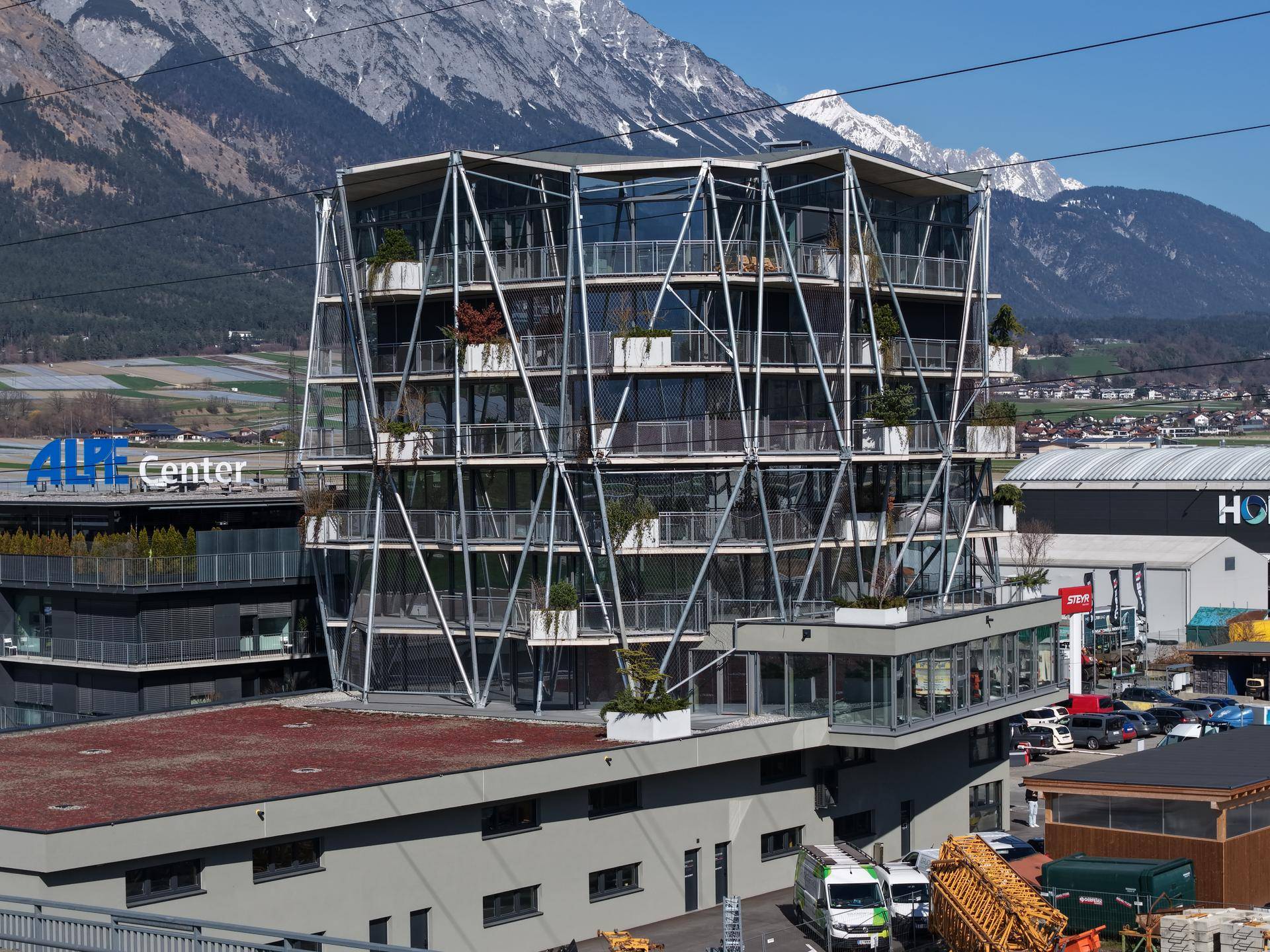 Auffälliges modernes Gebäude mit mehreren Etagen, großen Glasfronten und Balkonen, eingebettet in eine alpine Umgebung.