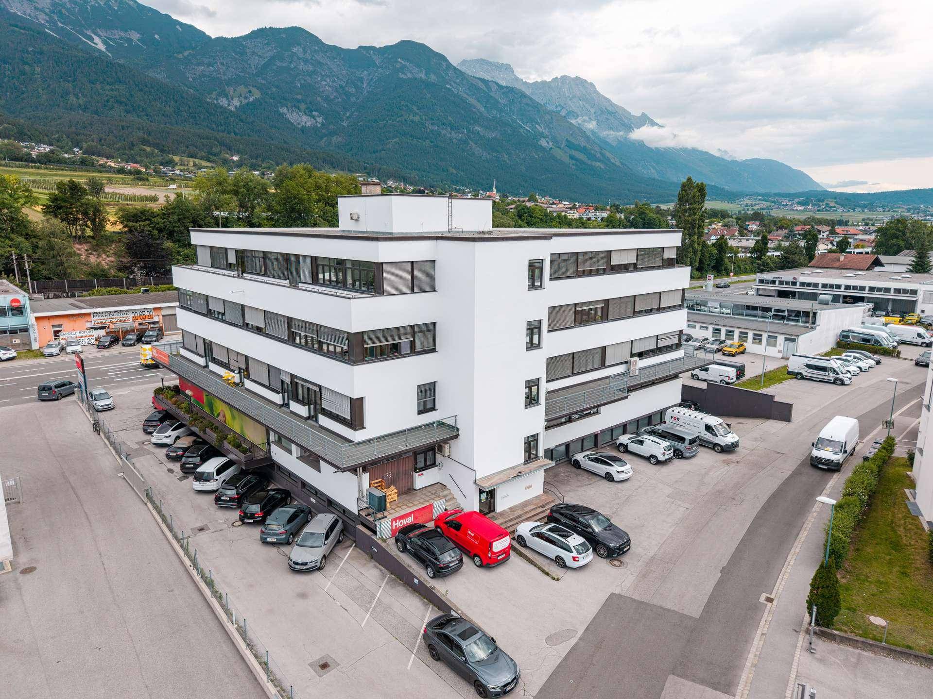 Luftaufnahme eines modernen Bürogebäudes mit Parkplätzen und beeindruckendem Bergpanorama.