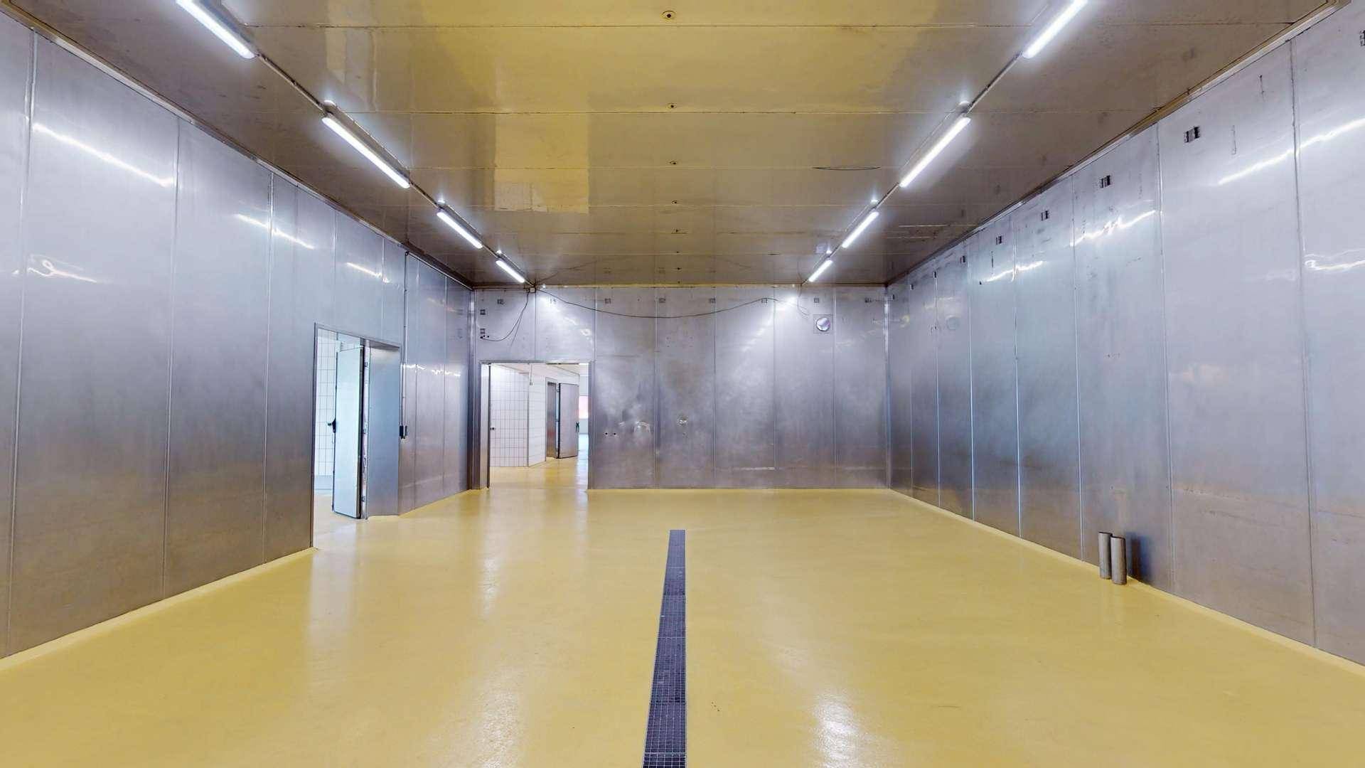 Industrieller Raum mit Metallverkleidung an den Wänden, hellem Boden und Deckenbeleuchtung.