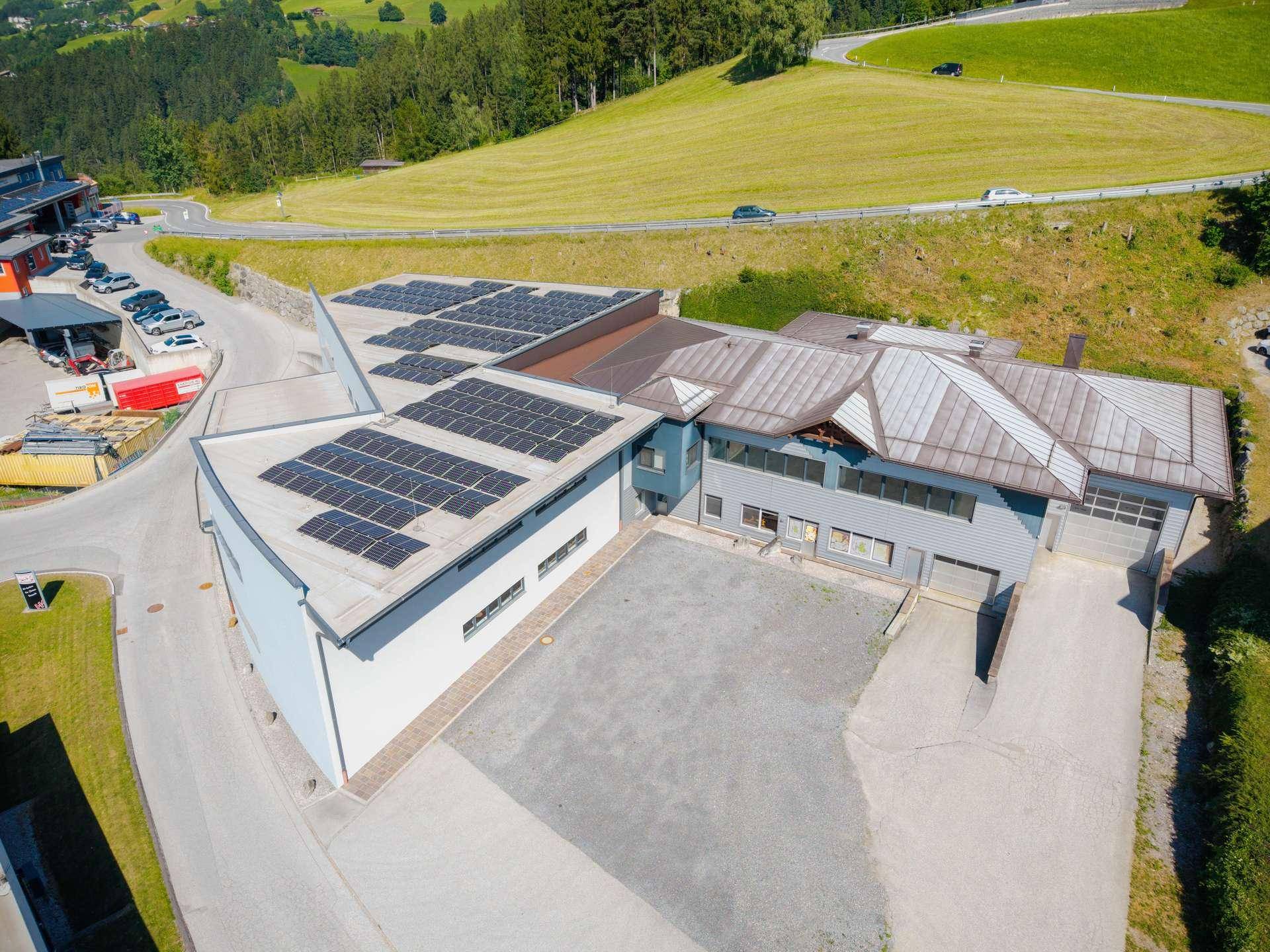 Luftaufnahme eines Gewerbegebäudes mit Solaranlagen auf dem Dach und angrenzenden Grünflächen.