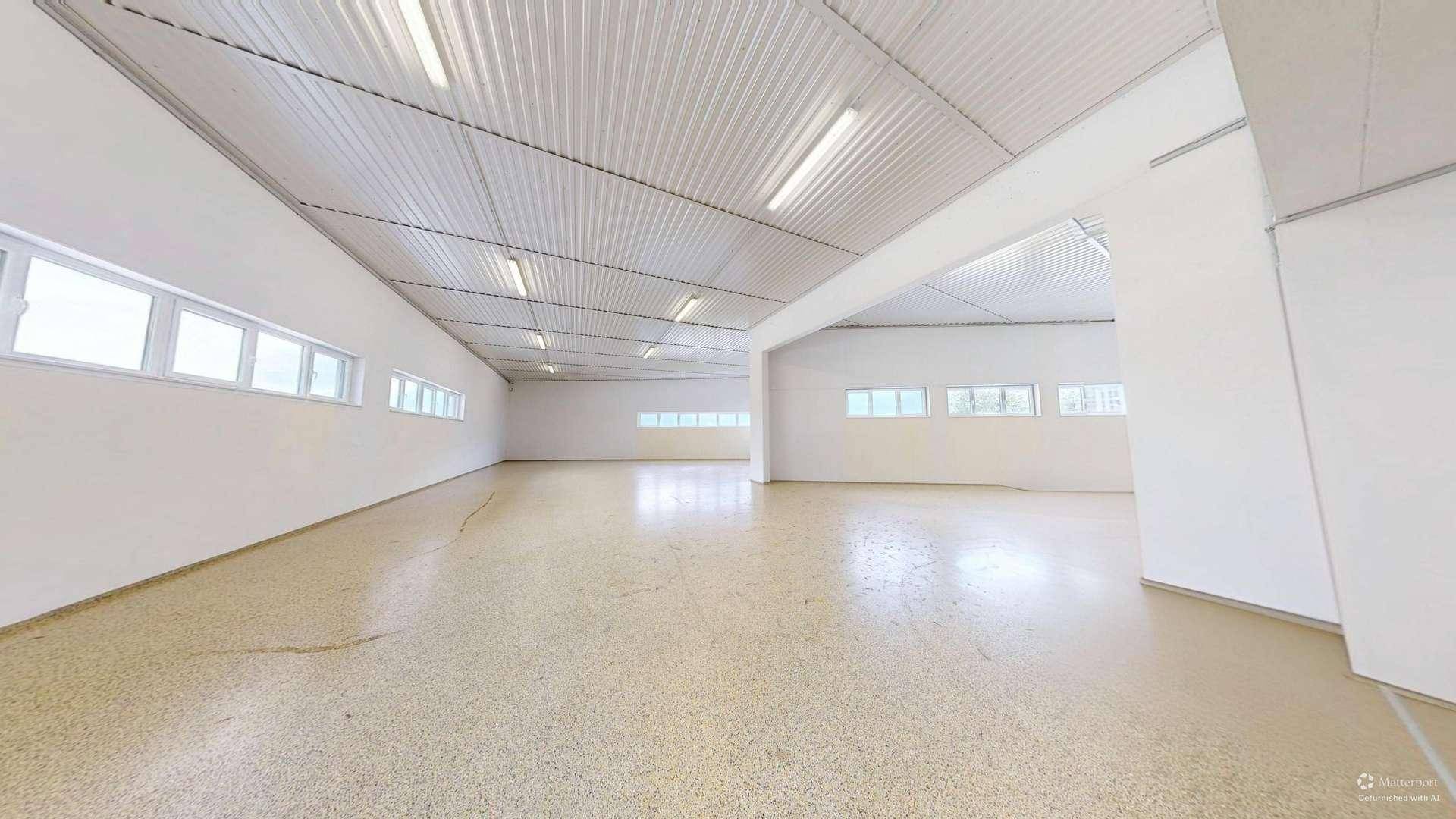 Großer, leerer Raum mit hohen Decken, vielen Fenstern und hellem Industrieboden.