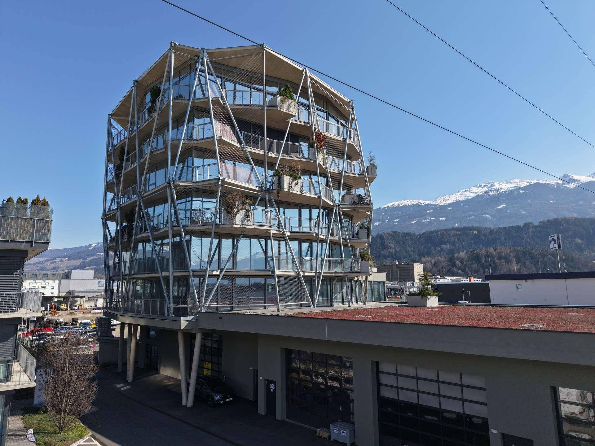 Innovatives Bürogebäude mit Glasfassade und Bergblick, umgeben von einer urbanen Landschaft.