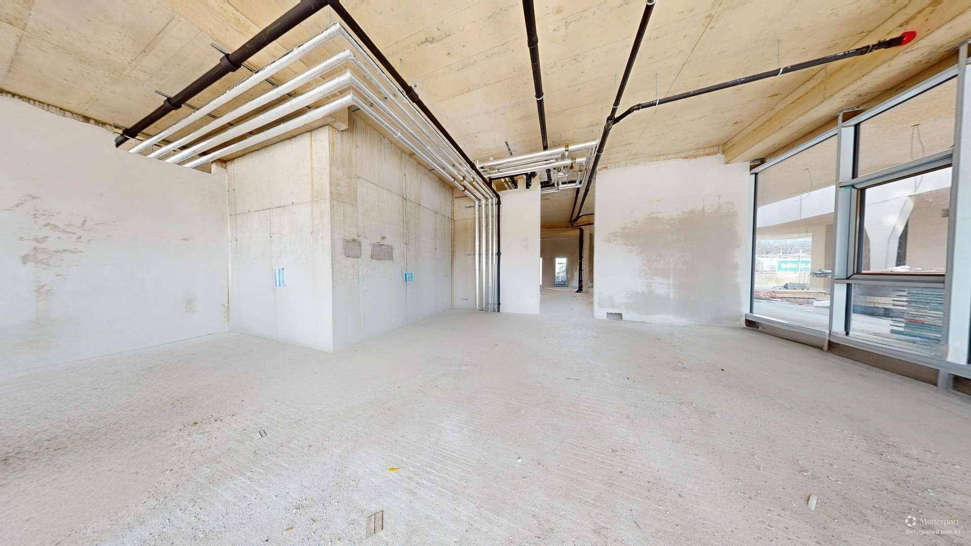 Rohbau eines Gewerberaums mit Betonwänden, sichtbaren Leitungen und großen Fenstern für viel Licht.