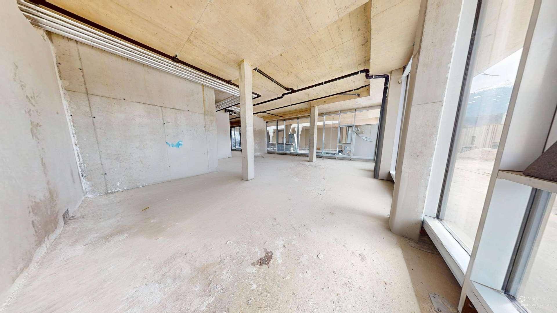 Heller Rohbau mit großen Fensterfronten, Betonstützen und sichtbaren Deckeninstallationen, ideal für individuelle Gestaltung.