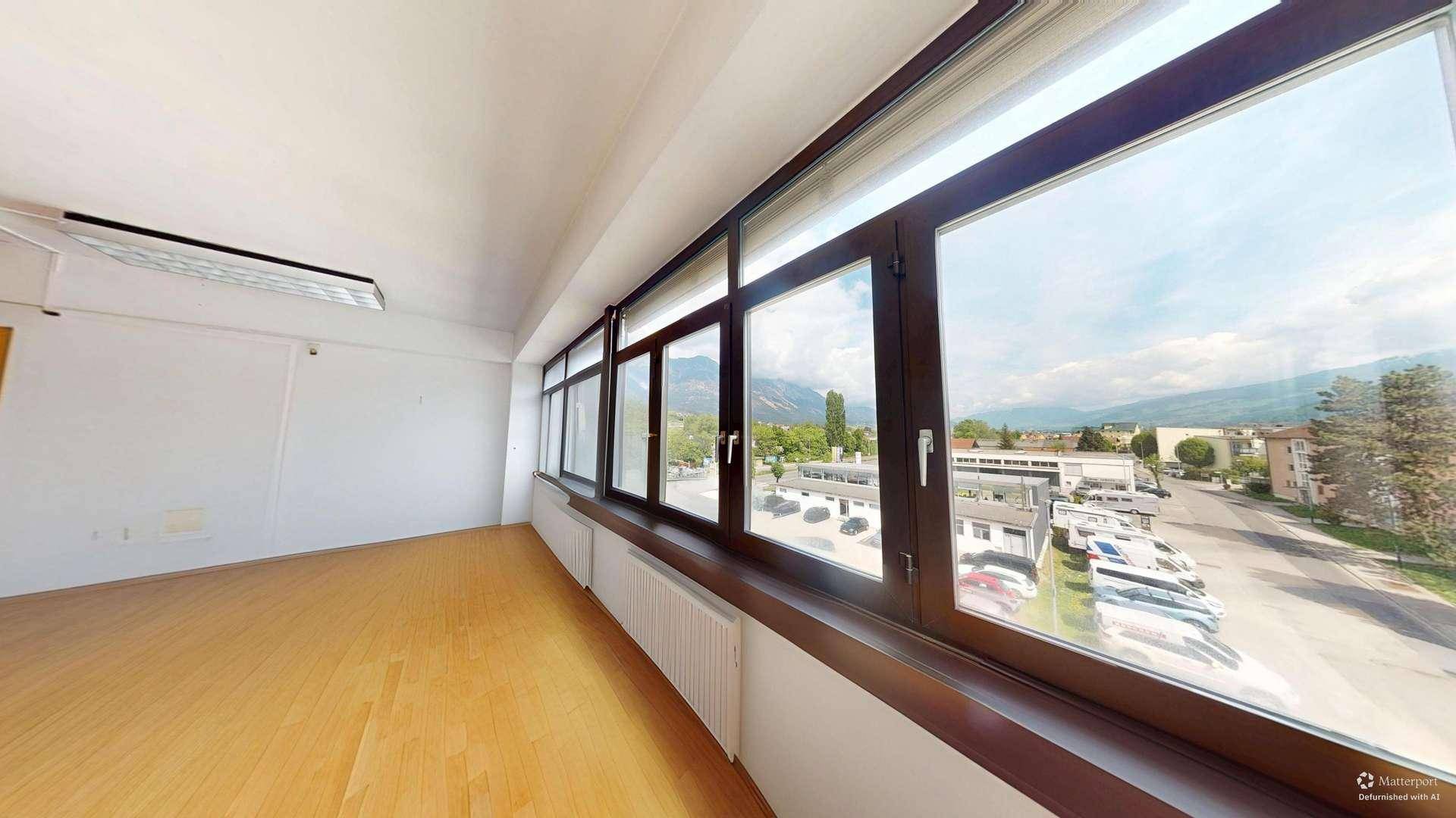 Heller Büroraum mit breiter Fensterfront, die einen weiten Blick auf die Berge und die Stadt bietet.