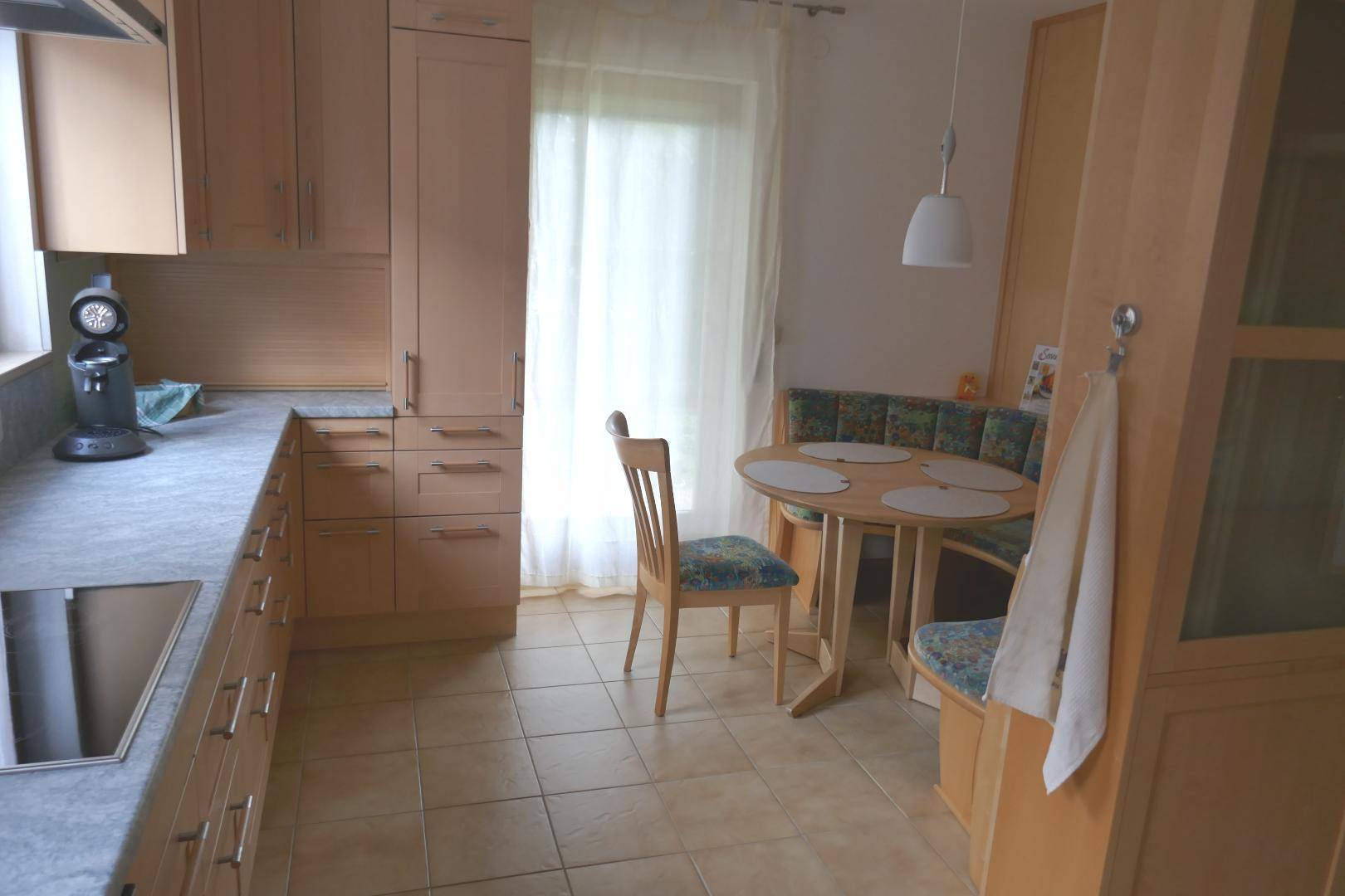 Gemütliche Küche mit heller Holzeinrichtung, Fliesenboden und einer praktischen Essecke am Fenster.
