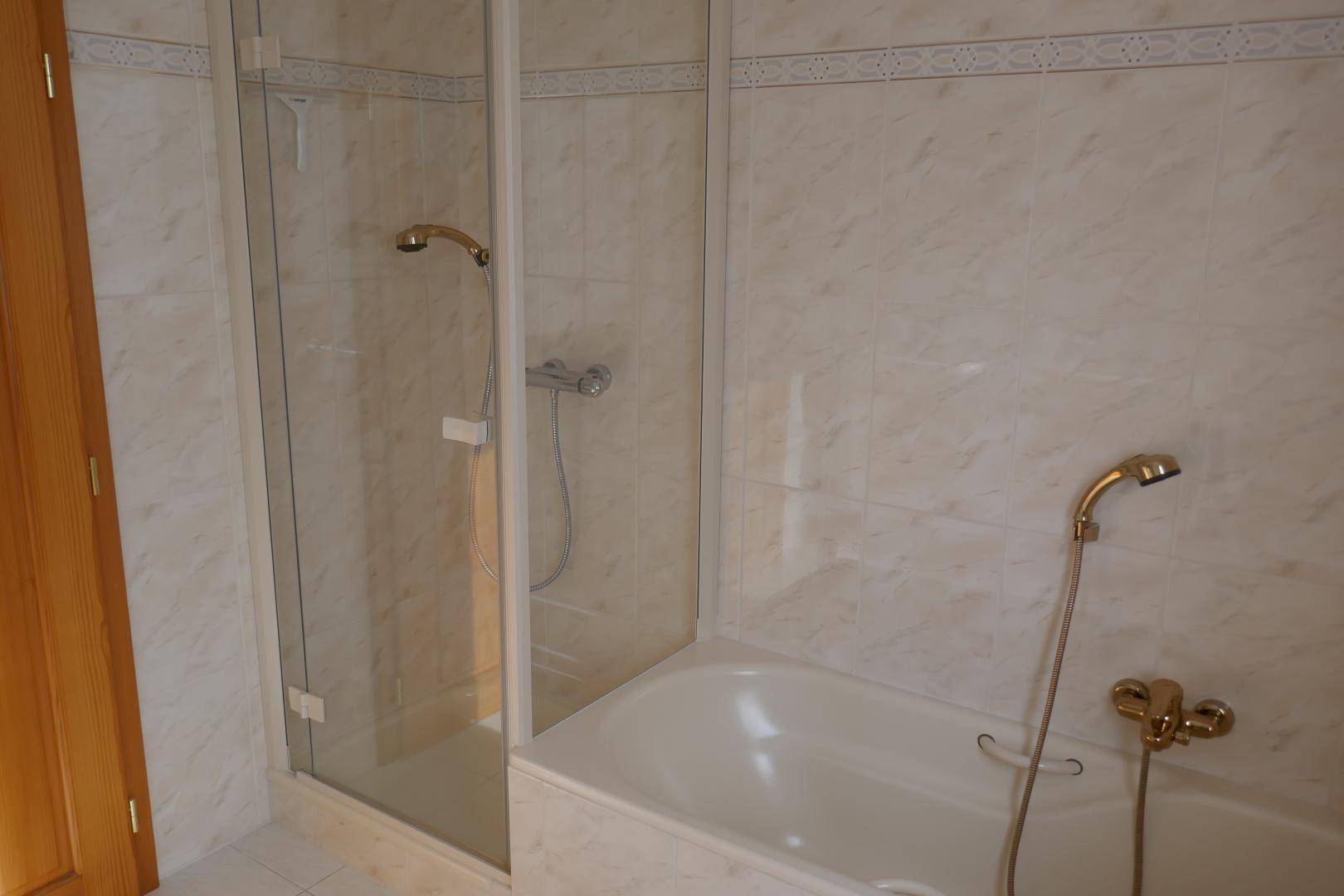 Badezimmer mit Badewanne und separater Duschkabine, komplett mit hellen Fliesen ausgestattet.