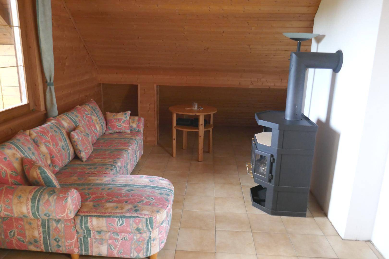 Gemütliches Wohnzimmer im Dachgeschoss mit Holzbalken, Sofa und einem modernen Holzofen für behagliche Wärme.