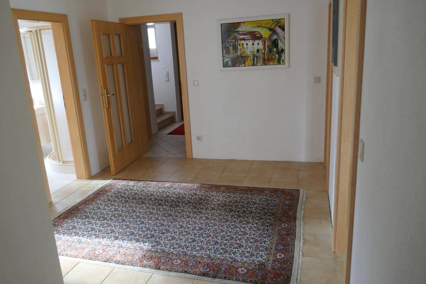 Heller Flur mit Fliesenboden und Holztüren, der zu verschiedenen Räumen und einer Treppe führt.