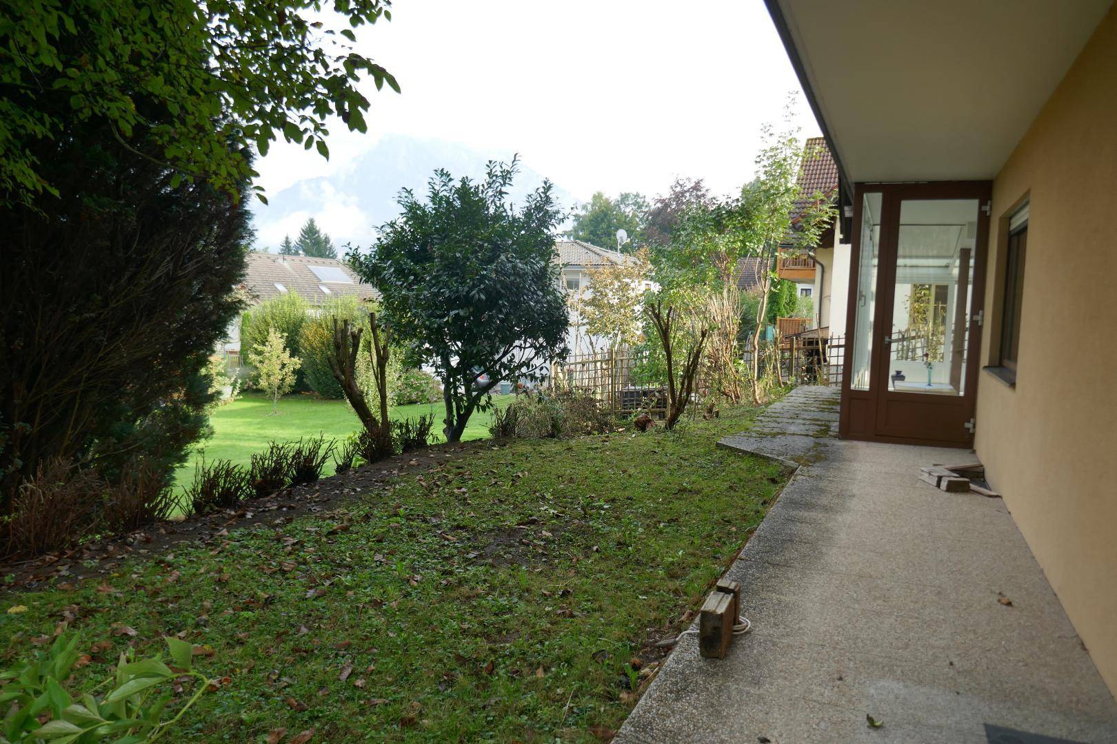 Abfallender Gartenbereich neben dem Haus mit gepflastertem Weg und Blick auf die umliegende Nachbarschaft.