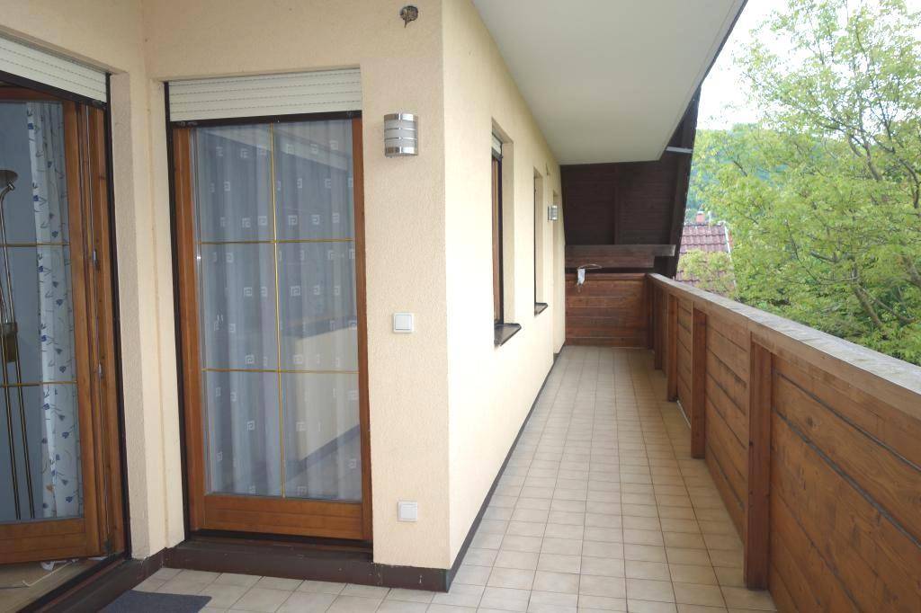 Langer Balkon mit Fliesenboden und Holzgeländer, der Zugang zu den Innenräumen bietet und Ausblick gewährt.
