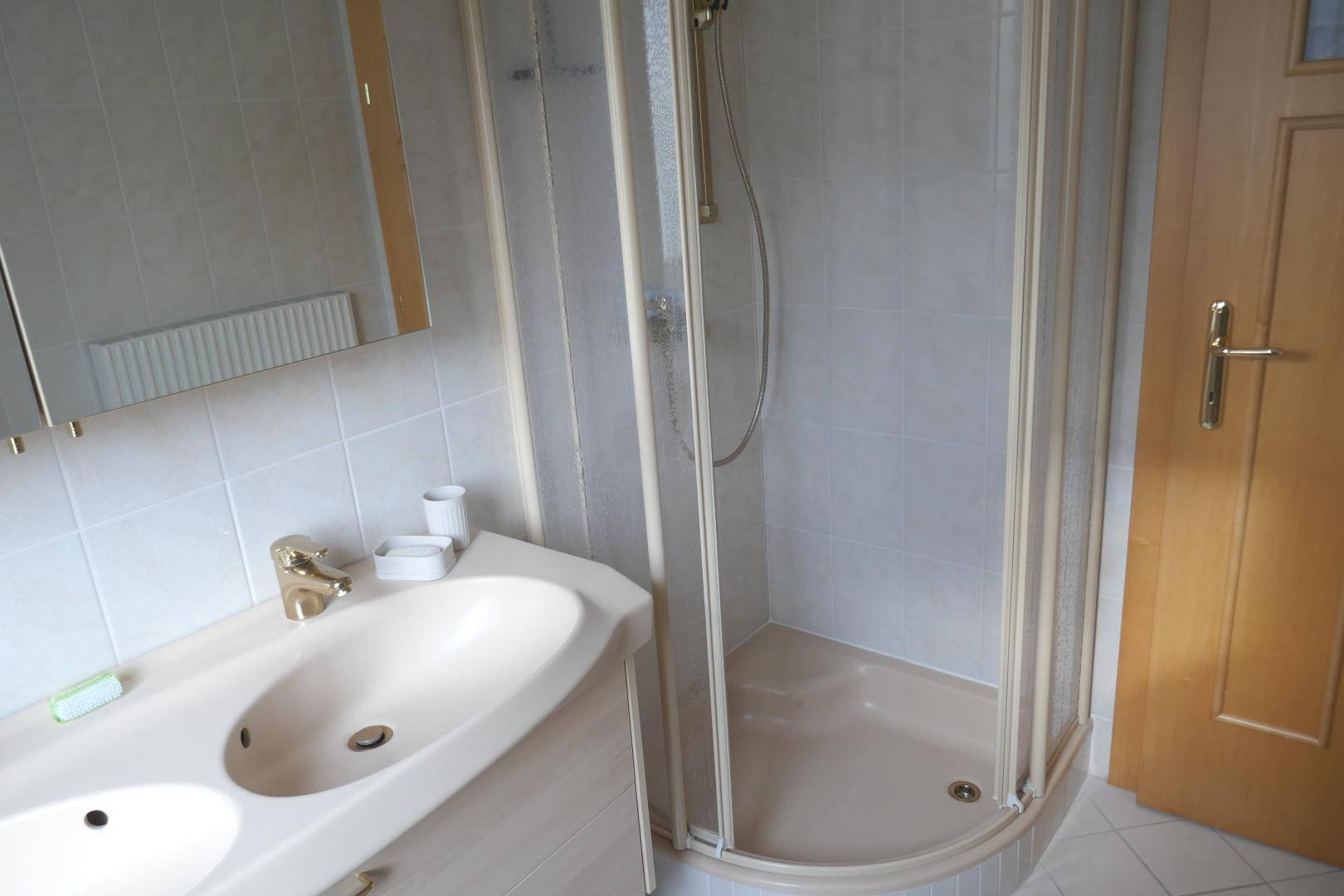 Funktionales Badezimmer mit Duschkabine, Einzelwaschbecken und Spiegelschrank, komplett gefliest.