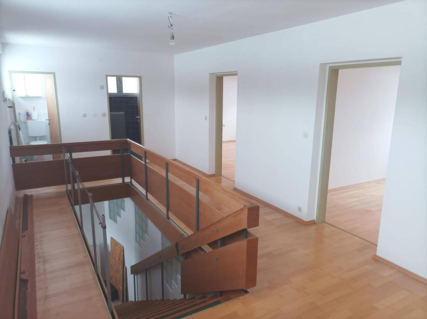 Geräumiger Flur mit Holztreppe, Geländer und Zugang zu verschiedenen Zimmern.