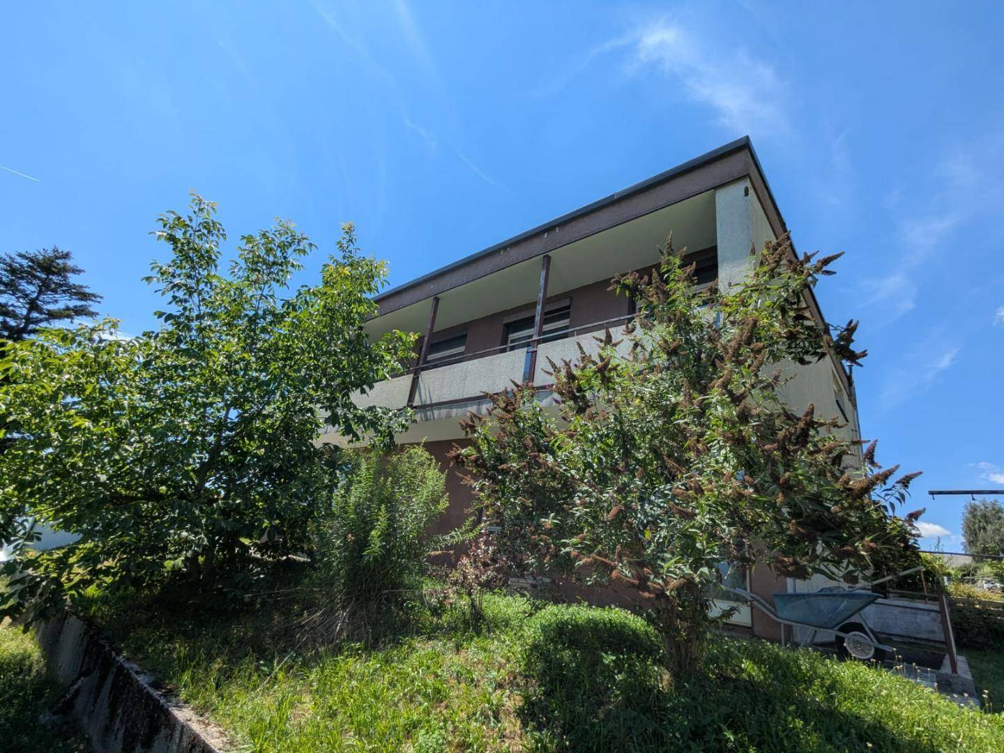 Ansicht des Hauses von der Seite, teilweise von Bäumen verdeckt, mit sichtbarem Balkon.