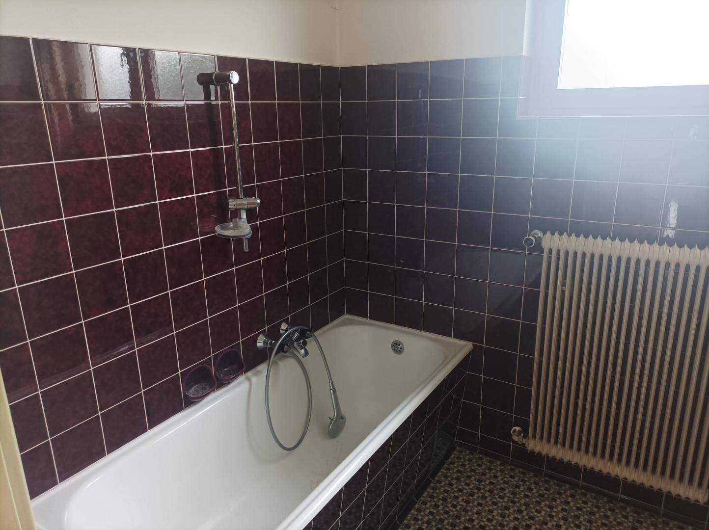 Badezimmer mit dunkelroten Fliesen, Badewanne, Duschvorrichtung und Fenster.