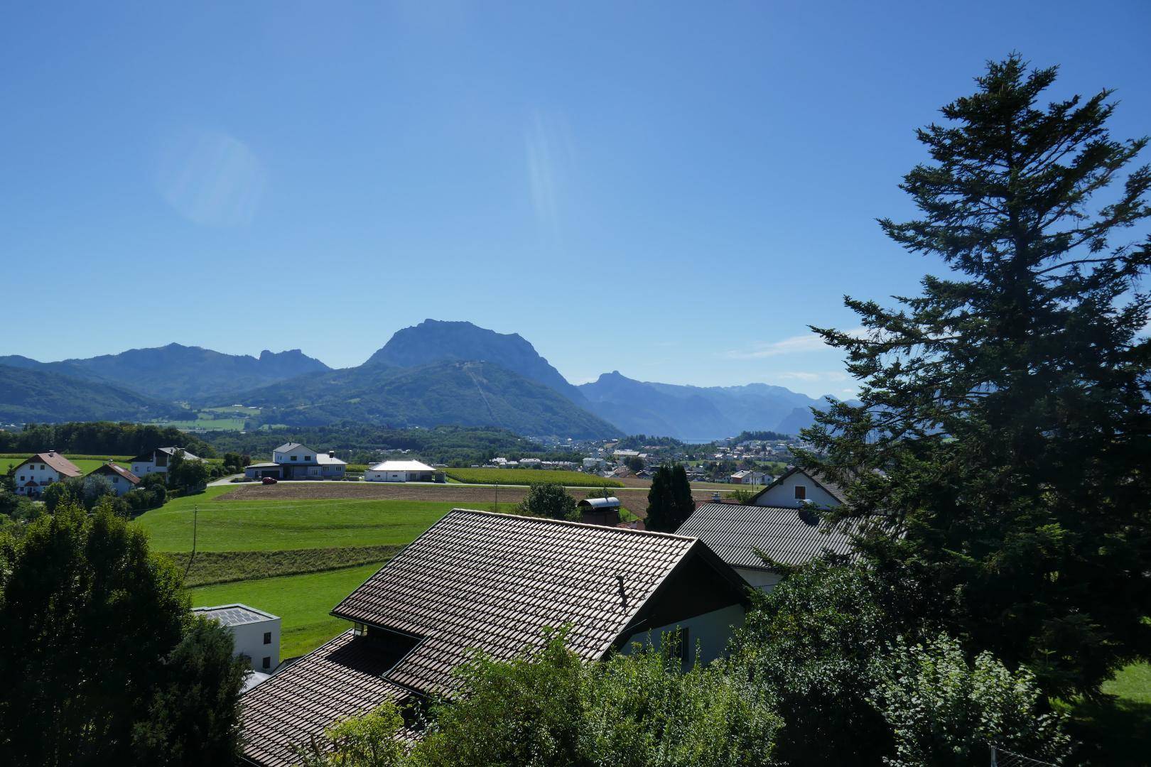 Weitläufiger Panoramablick auf die umliegende Berglandschaft, grüne Felder und Siedlungshäuser.