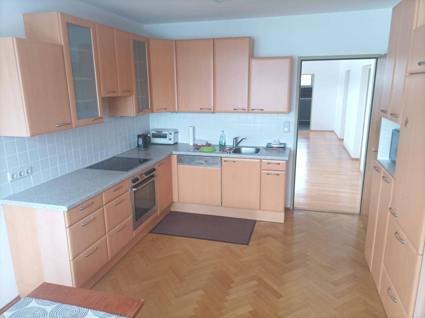 Funktionale Küche mit hellen Holzschränken, Einbaugeräten und Fischgrätparkettboden.