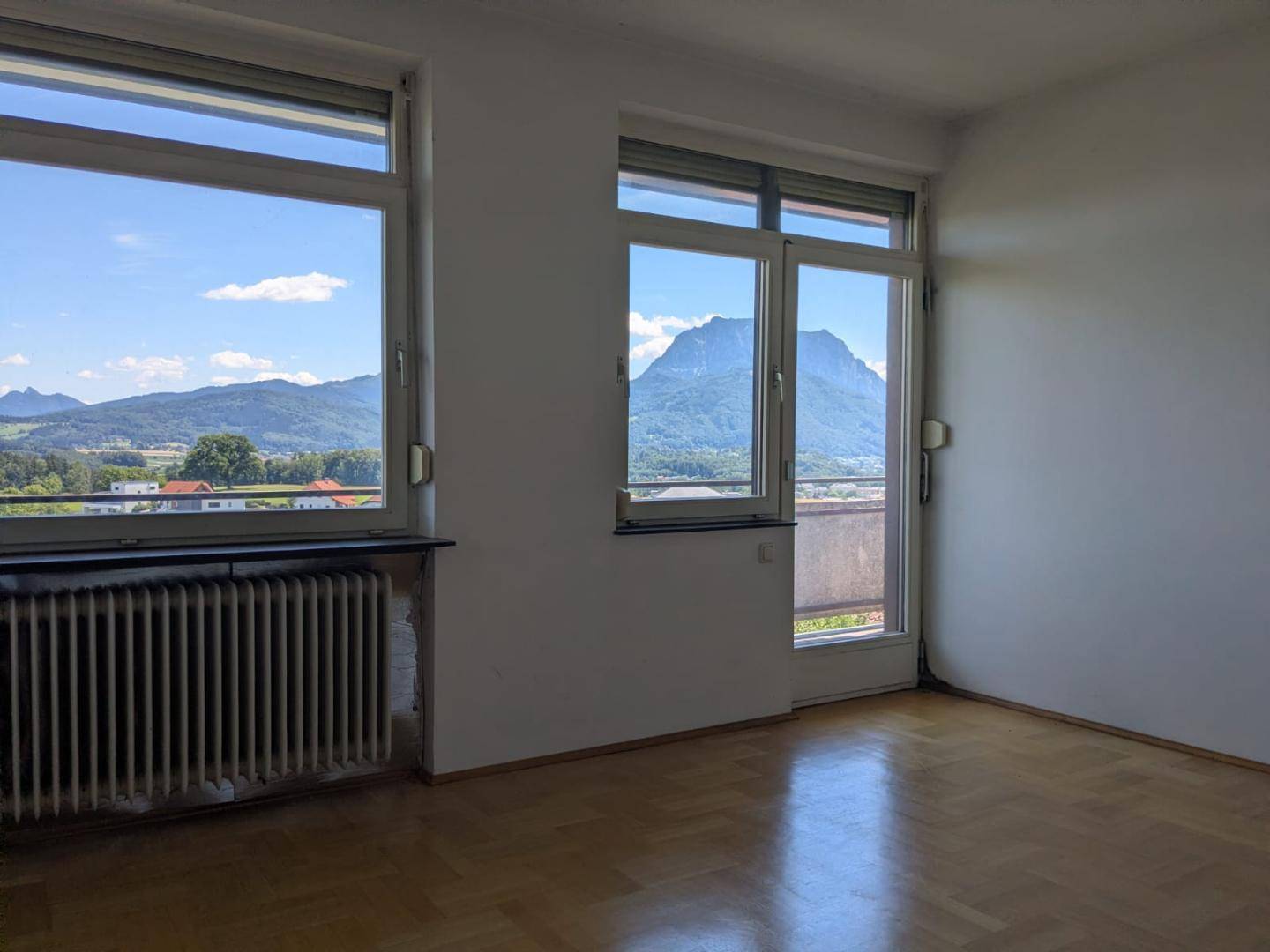 Heller Raum mit großen Fenstern, Parkettboden und beeindruckendem Bergblick.