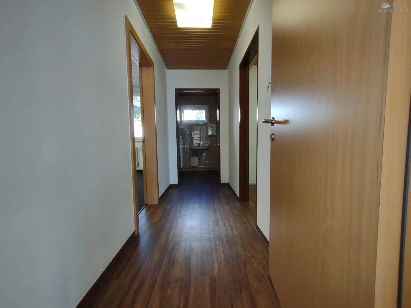 Langer Flur mit Laminatboden und Holzdecke, der zu verschiedenen Räumen führt.