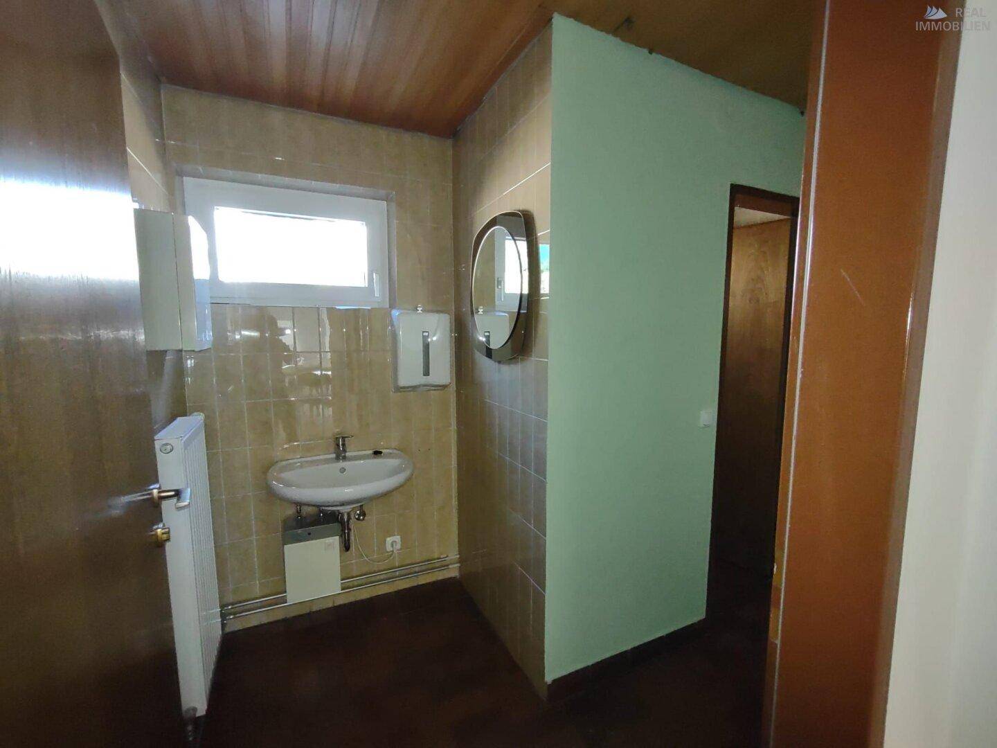 Kleiner WC-Raum mit Fliesen an den Wänden, Waschbecken und Fenster für Tageslicht.