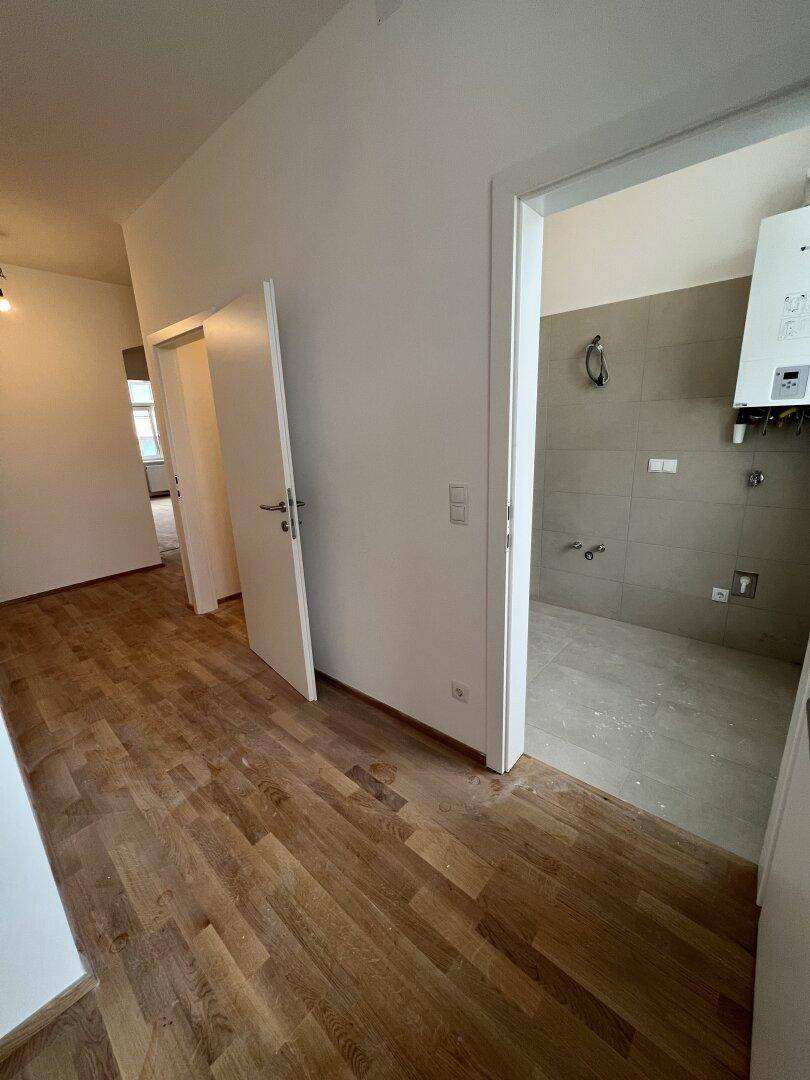Langer Flur mit Holzboden und Zugang zu verschiedenen Räumen, inklusive einem vorbereiteten Badbereich.